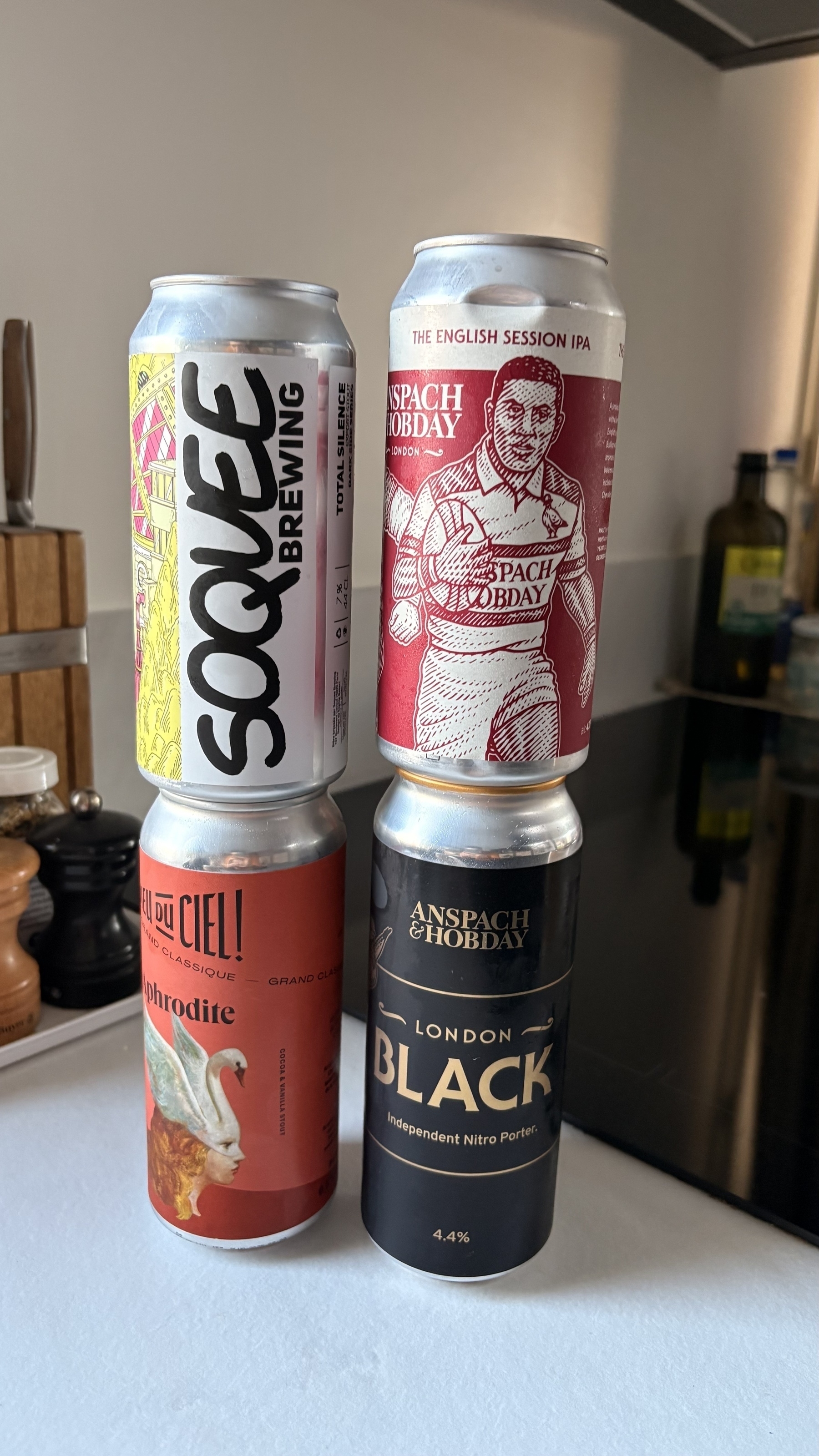 Four beer cans are stacked on a kitchen countertop, each featuring distinct and colorful designs.