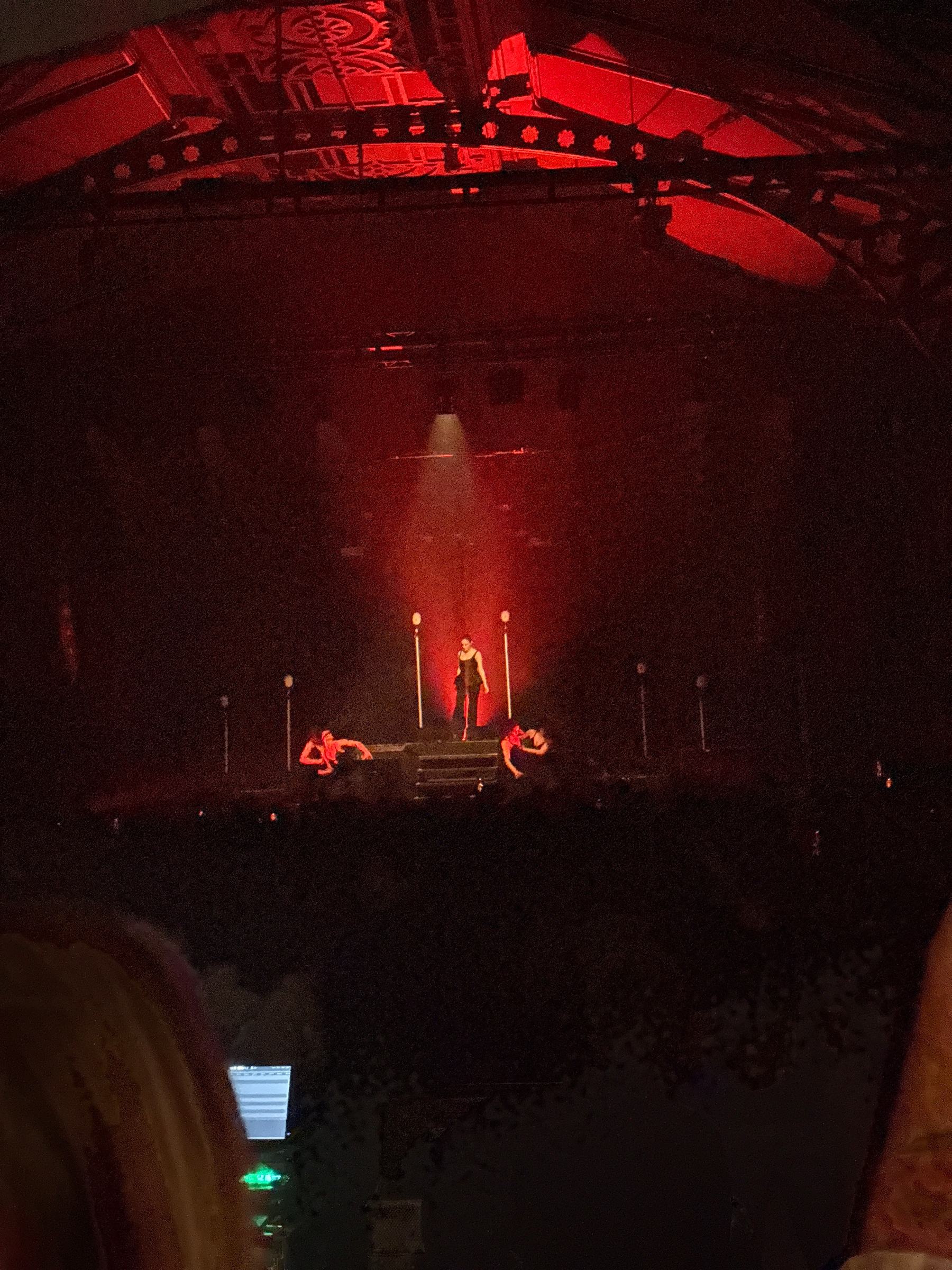 A performer is on stage under dramatic red lighting, surrounded by dancers.