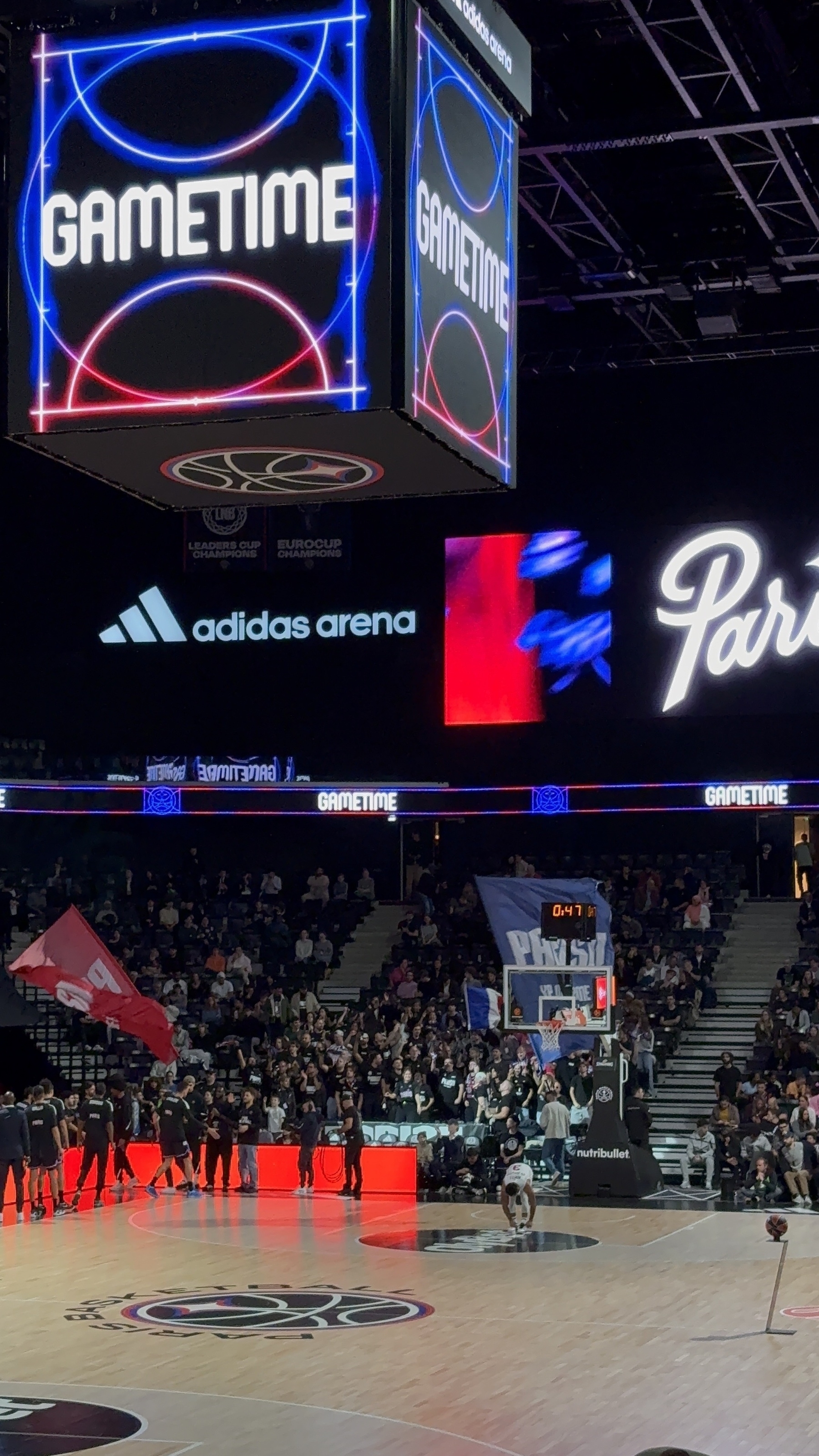 A basketball court is set up in an arena with a large screen displaying GAMETIME, surrounded by a crowd and various advertisements.