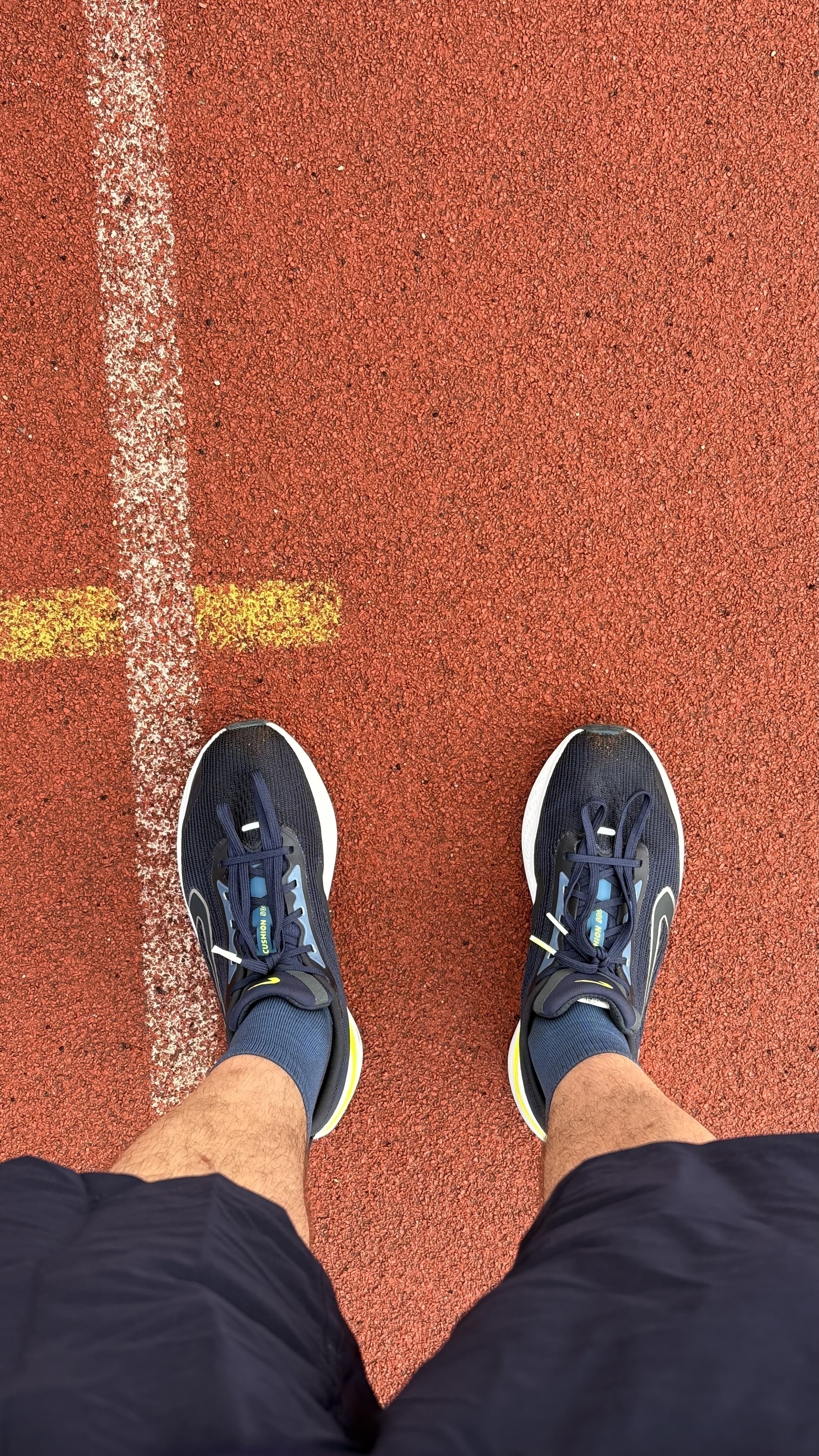 A person wearing running shoes stands on a red track, facing a yellow line.