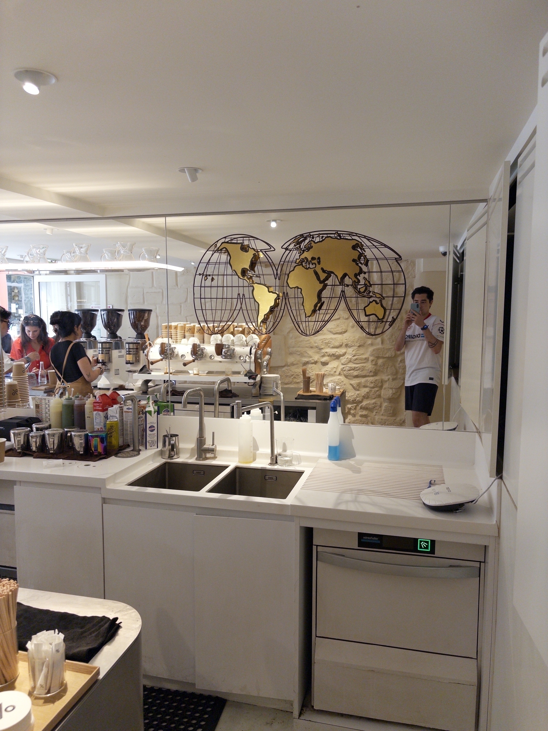People are gathered in a bright, modern café with a mirror displaying a decorative world map on the wall.