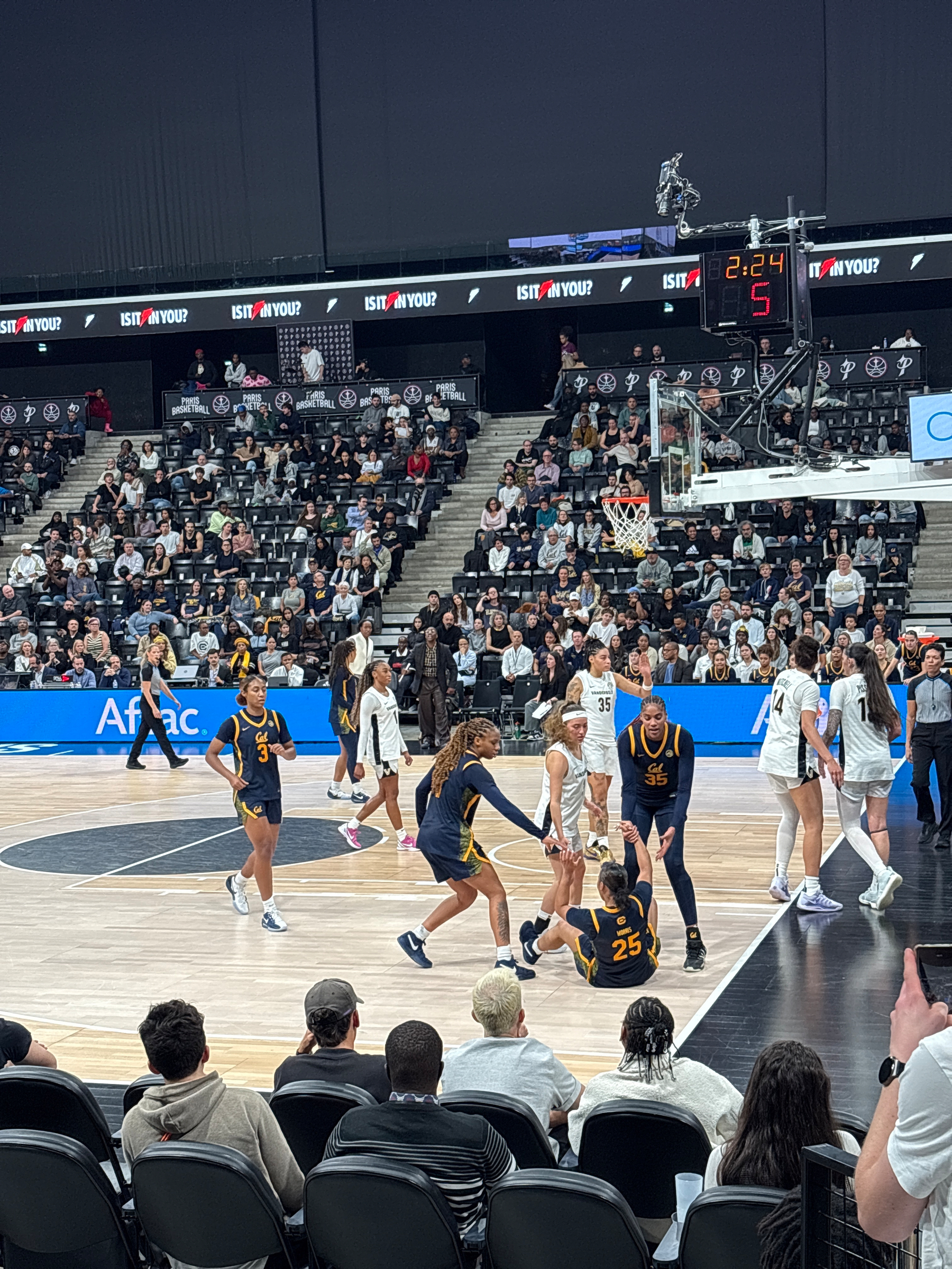 A women's basketball game is underway with players actively engaging on the court, watched by a seated audience.