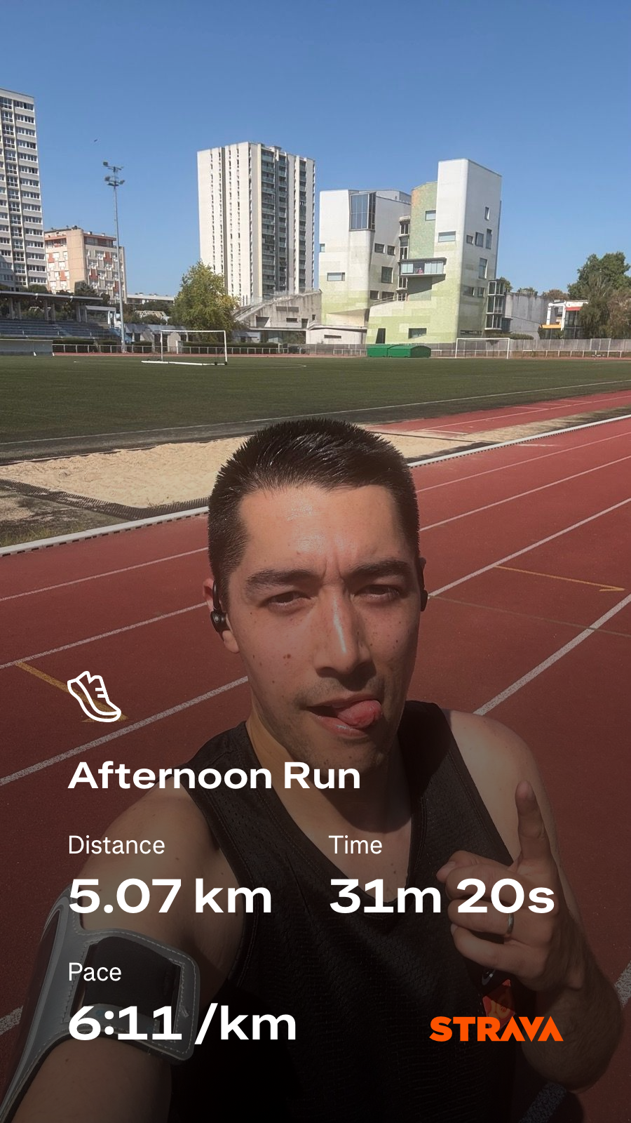 A person is taking a selfie on a track, showing details of an afternoon run including the distance, time, and pace with buildings in the background.