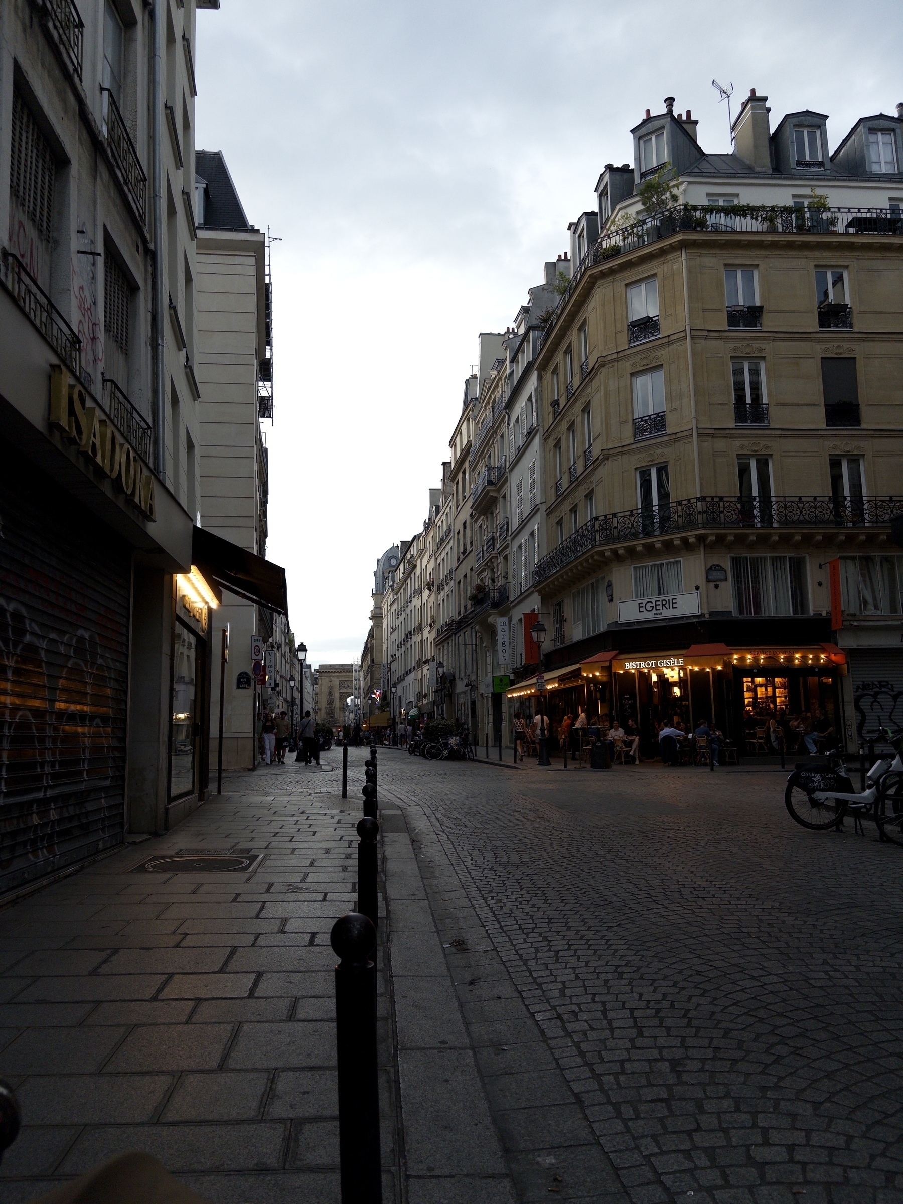 A narrow cobblestone street is lined with Parisian buildings and a café with glowing lights, creating a cozy atmosphere.