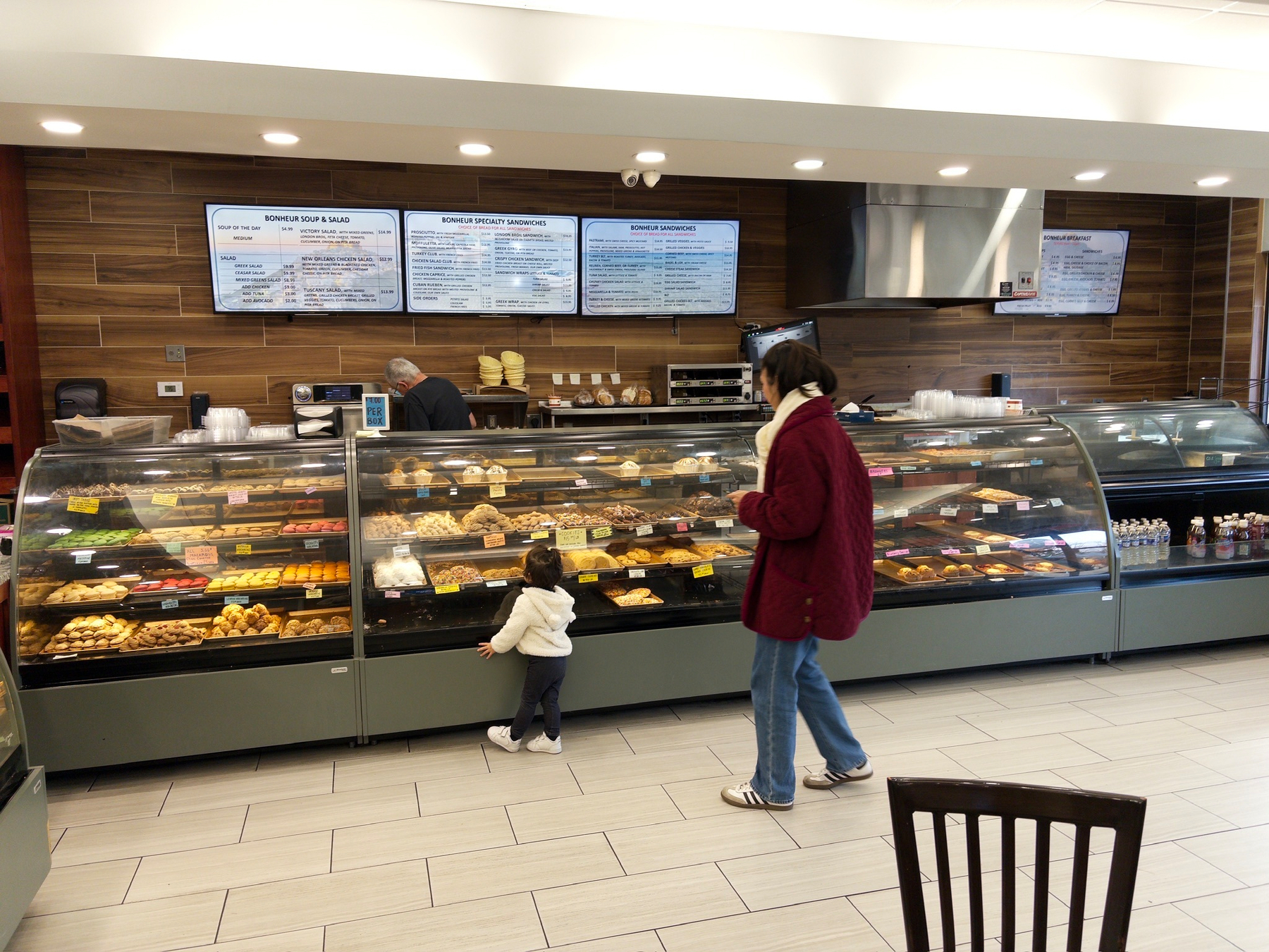 A woman and a child are standing in front of a bakery display filled with various pastries and sweets.