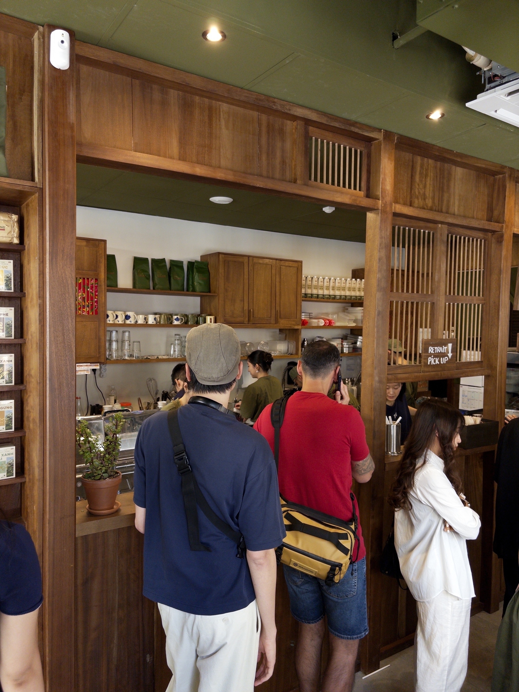 People are standing in line inside a wooden-themed cafe with shelves displaying various products.