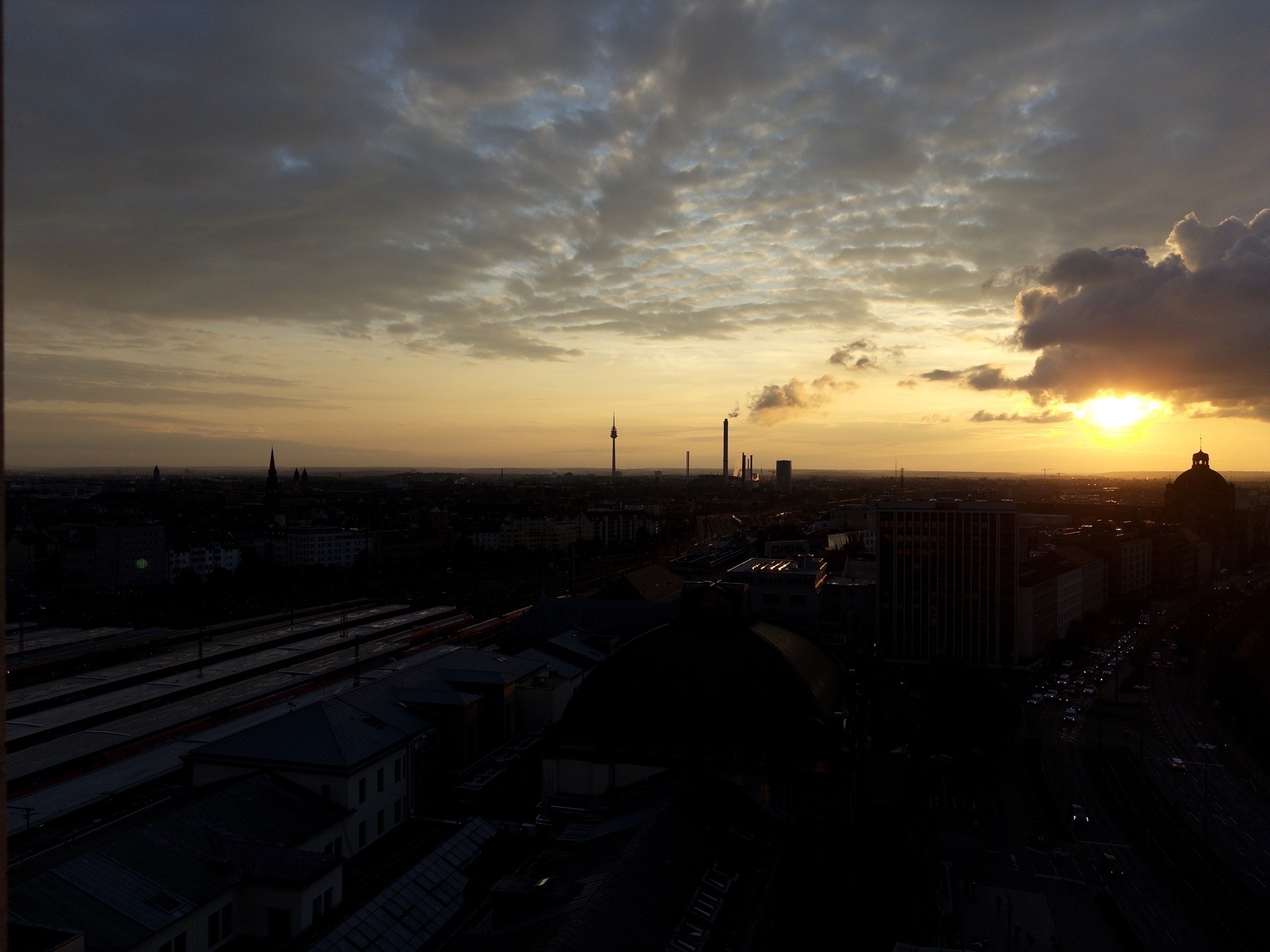 A cityscape at sunset features a skyline with tall structures silhouetted against a colorful sky.
