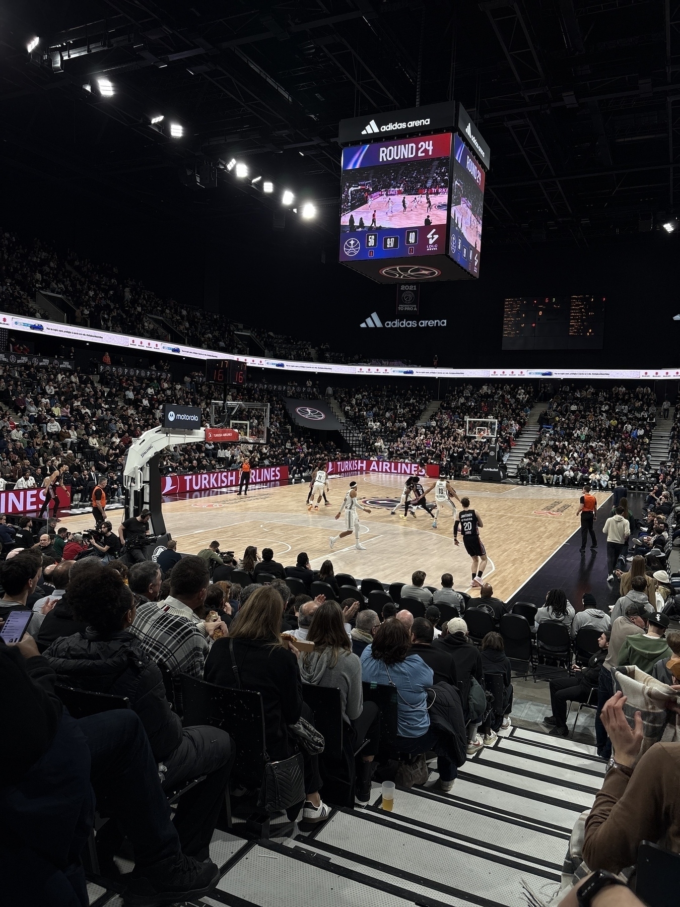 A basketball game is taking place in a crowded indoor arena, with the scoreboard displaying "Round 24."