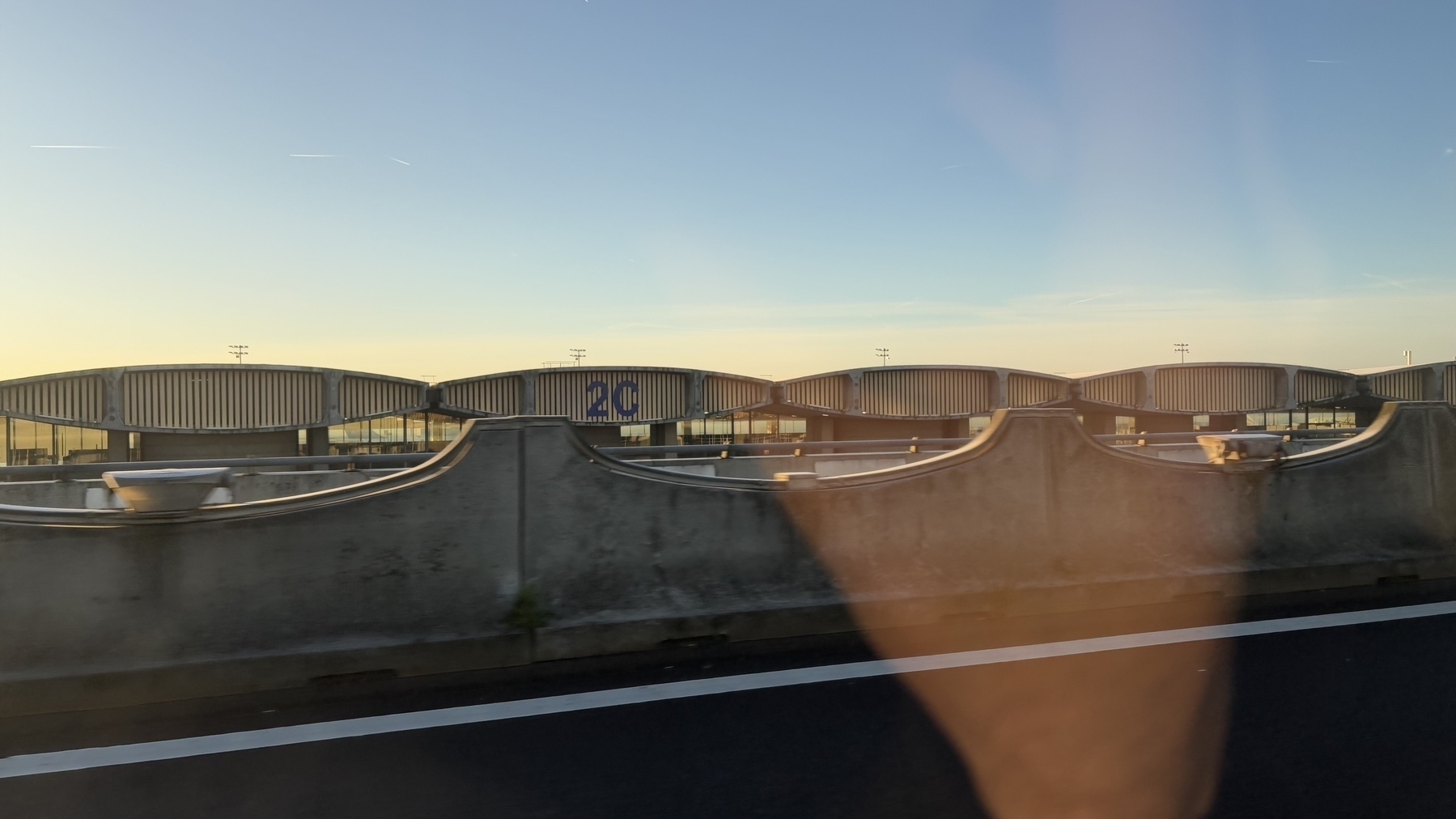 A view of a modern airport terminal with multiple sections, as seen from a nearby road.