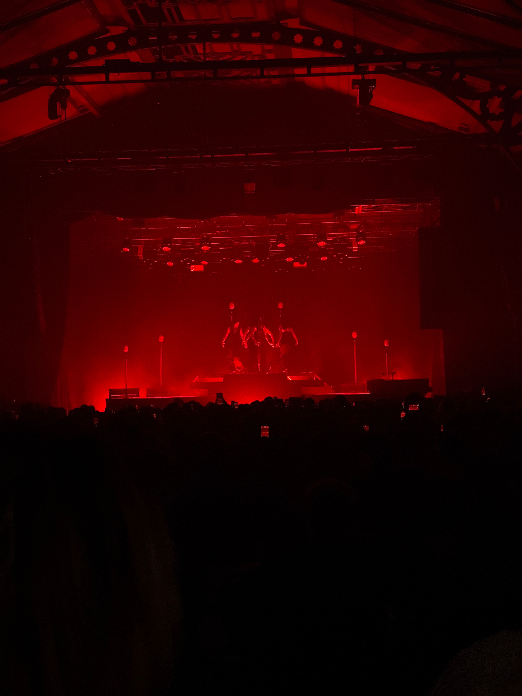 A dimly lit concert stage bathed in red light with performers silhouetted against the backdrop.