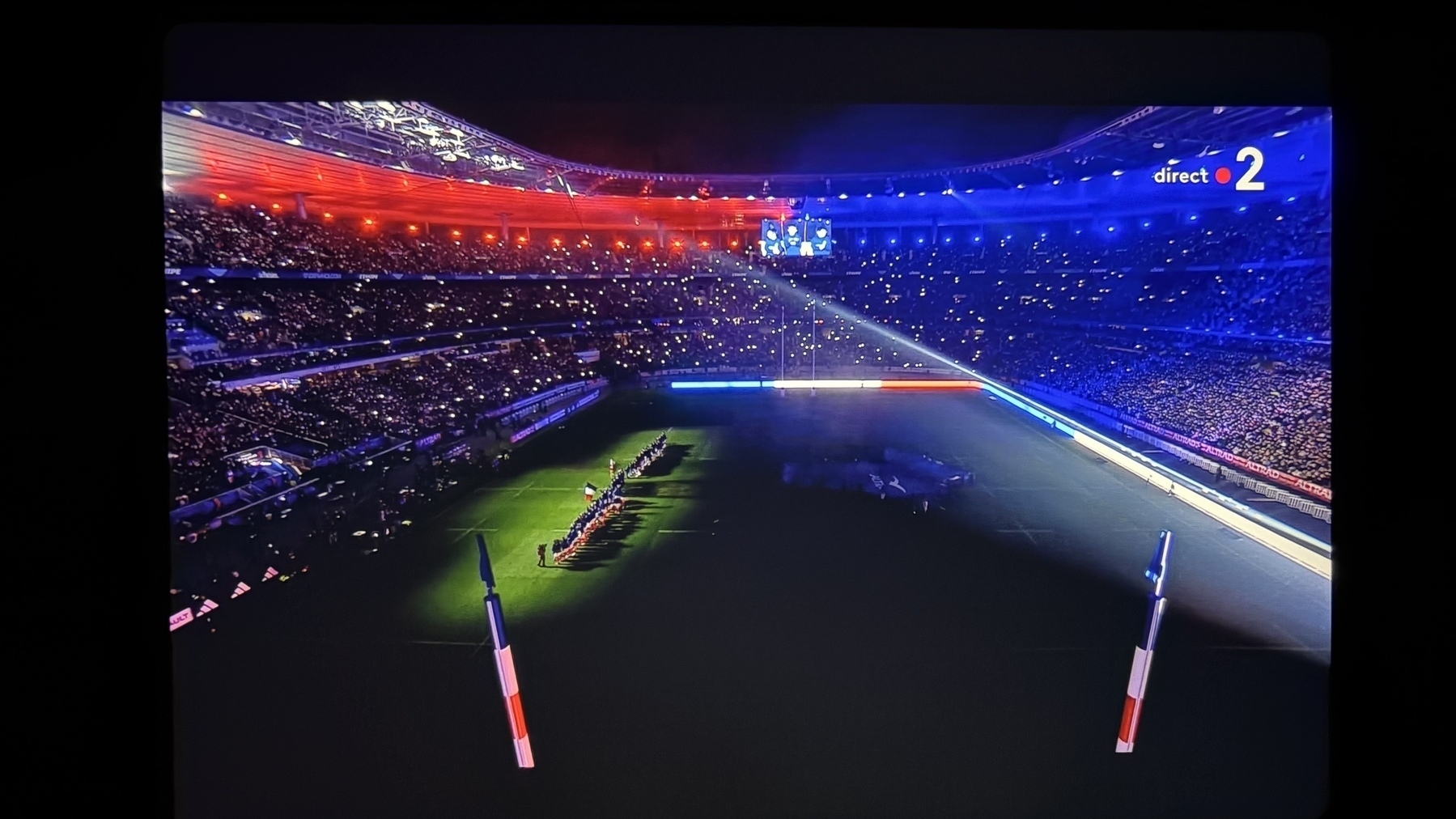 A stadium filled with spectators is illuminated by lights in the colors of the French flag, creating a vibrant and patriotic atmosphere.