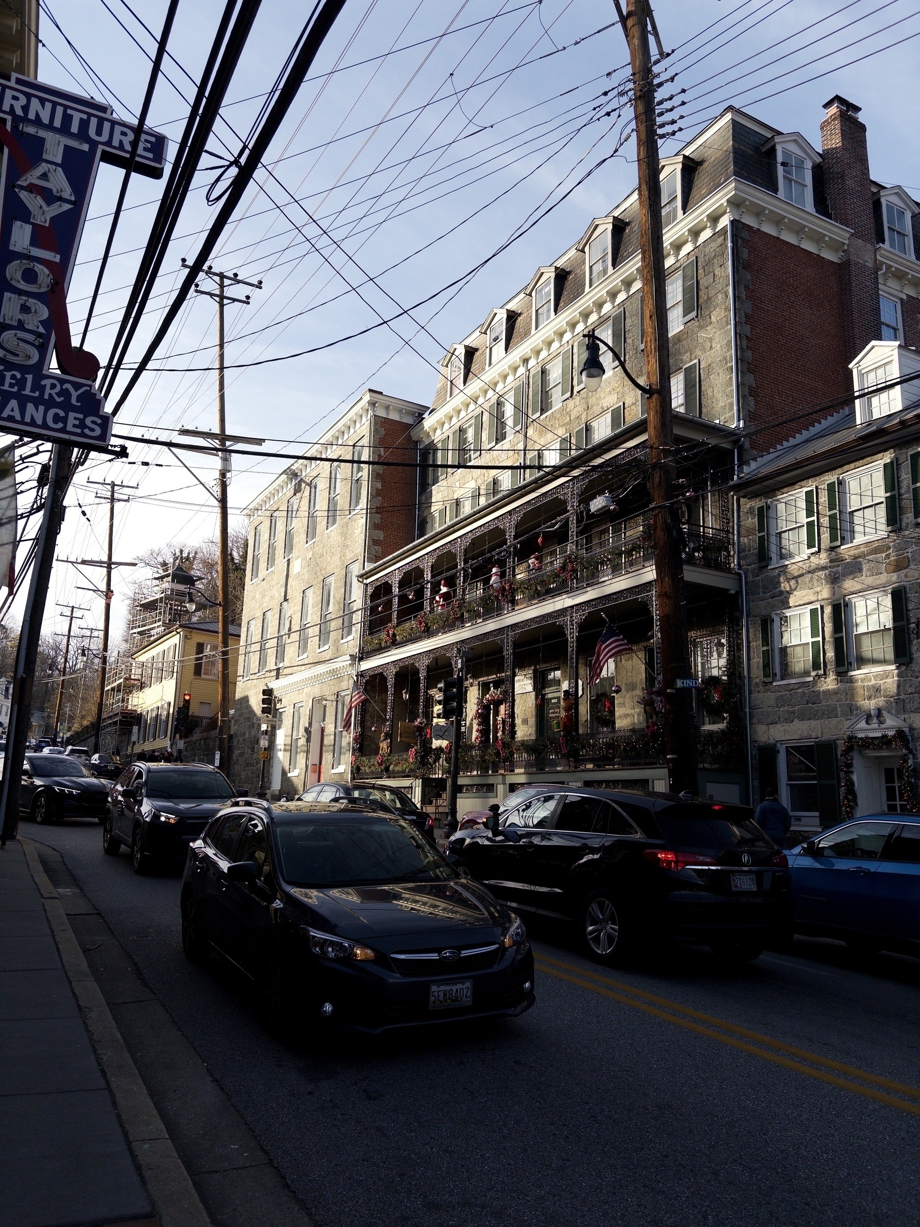 A busy street with several cars parked along a row of historic brick buildings adorned with festive decorations.