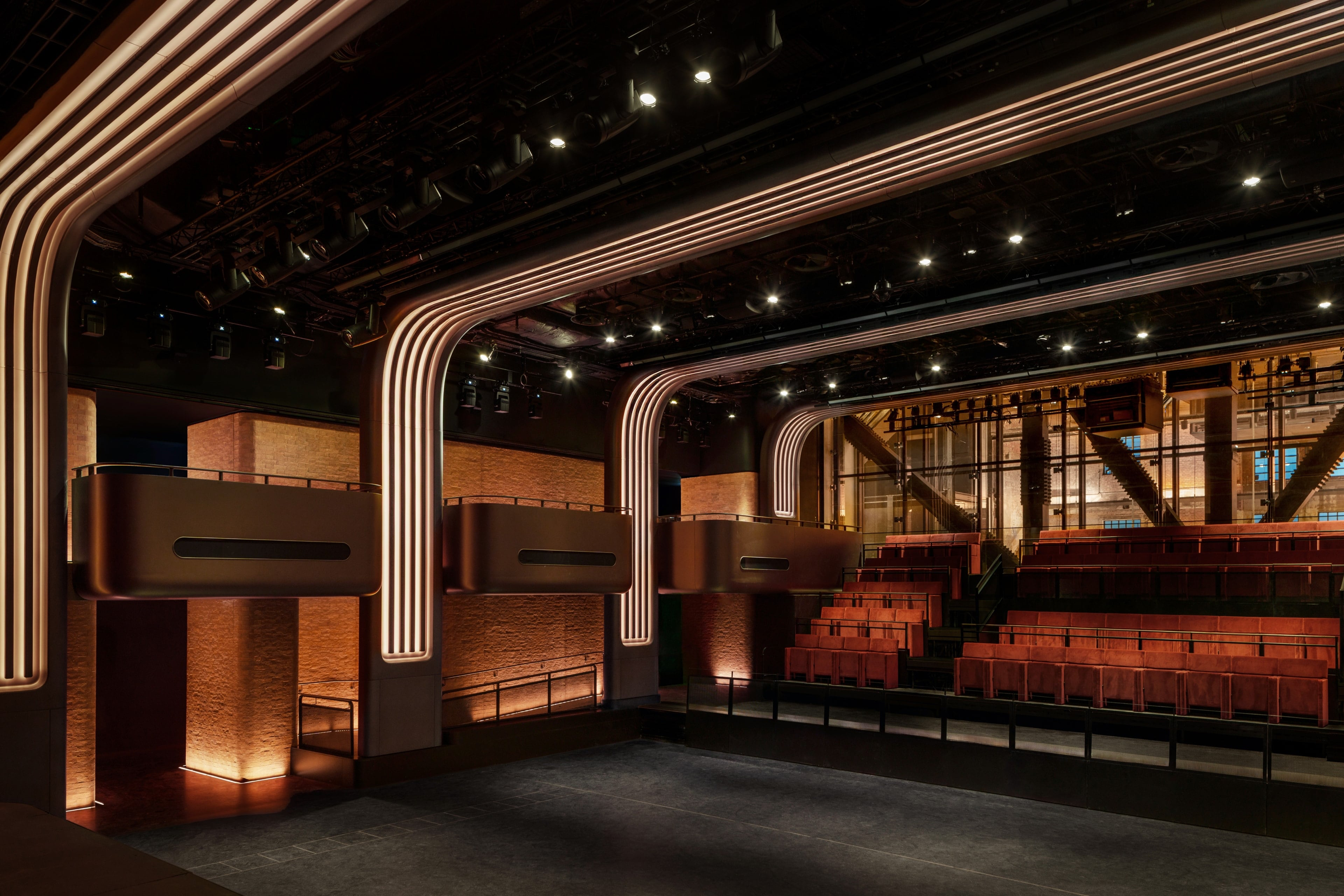 Auto-generated description: A modern theater interior features warm lighting, curved architectural elements, and tiered seating arrangements.
