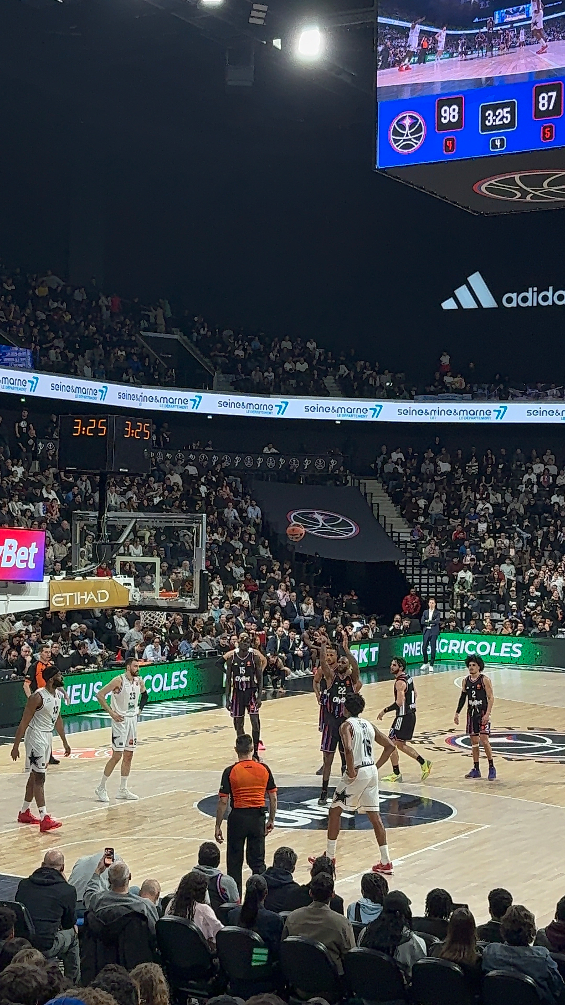 A basketball game is taking place in an indoor stadium with a crowd watching, and one team is attempting a free throw.