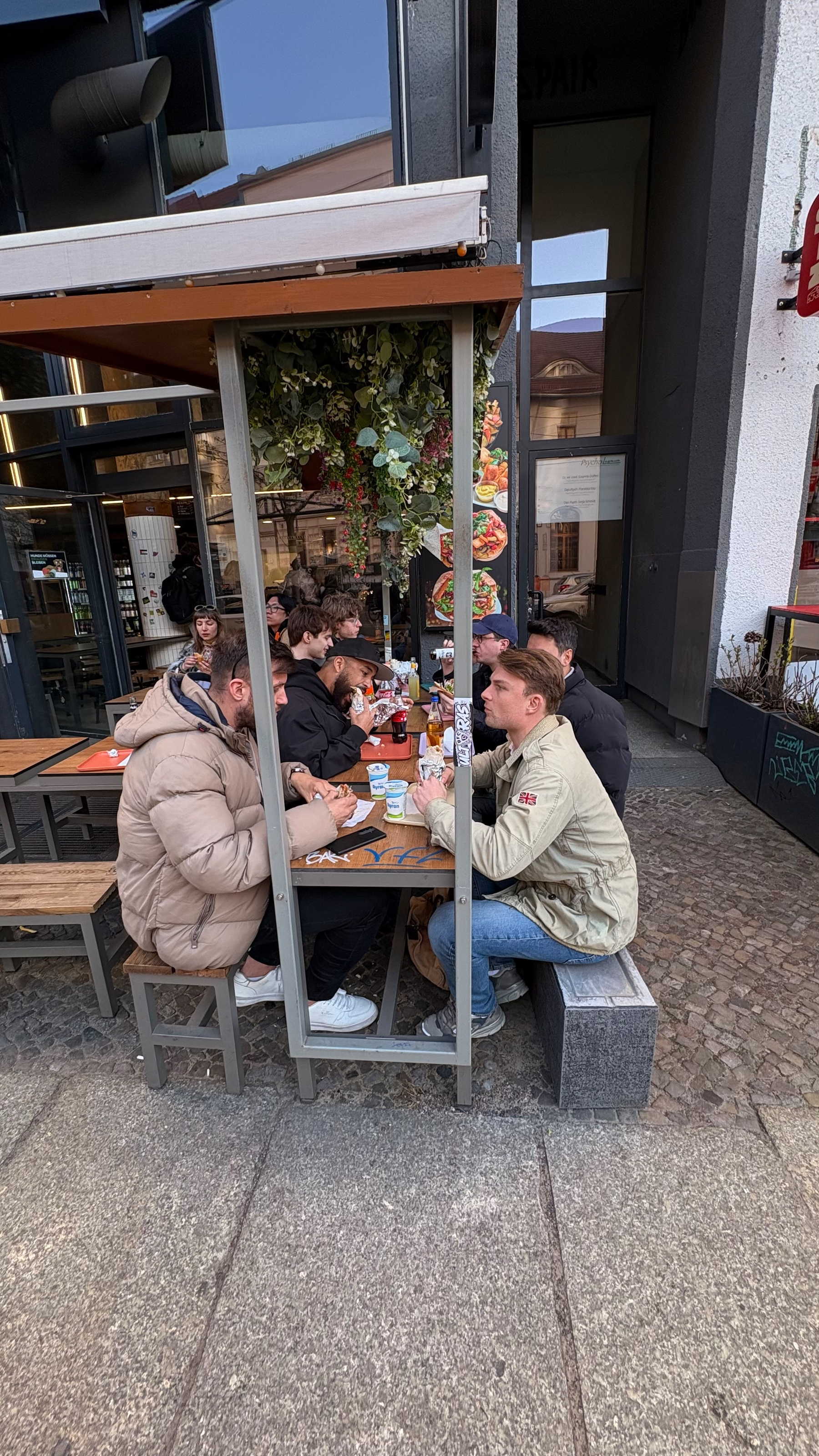 Auto-generated description: People are sitting at an outdoor table enjoying food and drinks at a cafe or restaurant.