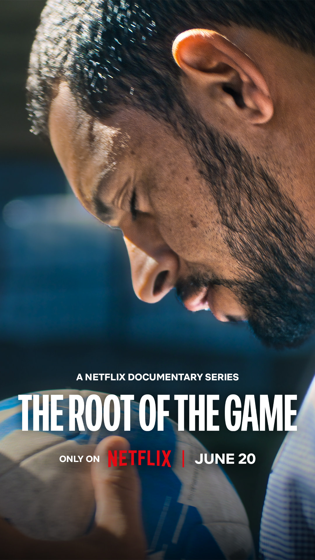 Auto-generated description: A close-up of a man intensely holding and looking down at a soccer ball is used as the promotional image for the Netflix documentary series The Root of the Game releasing on June 20.