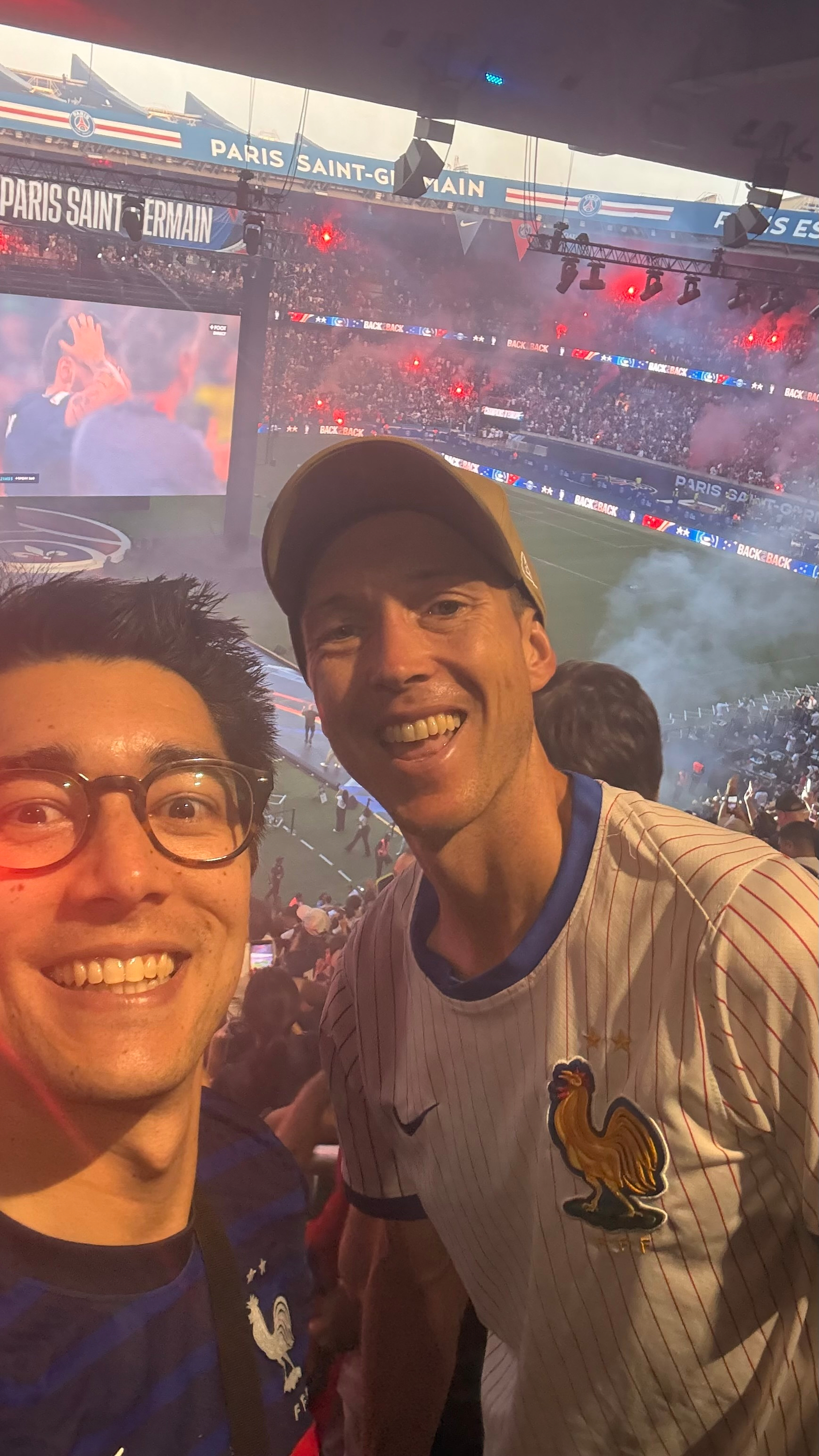 Two people are smiling in a stadium filled with spectators, possibly during a sports event.