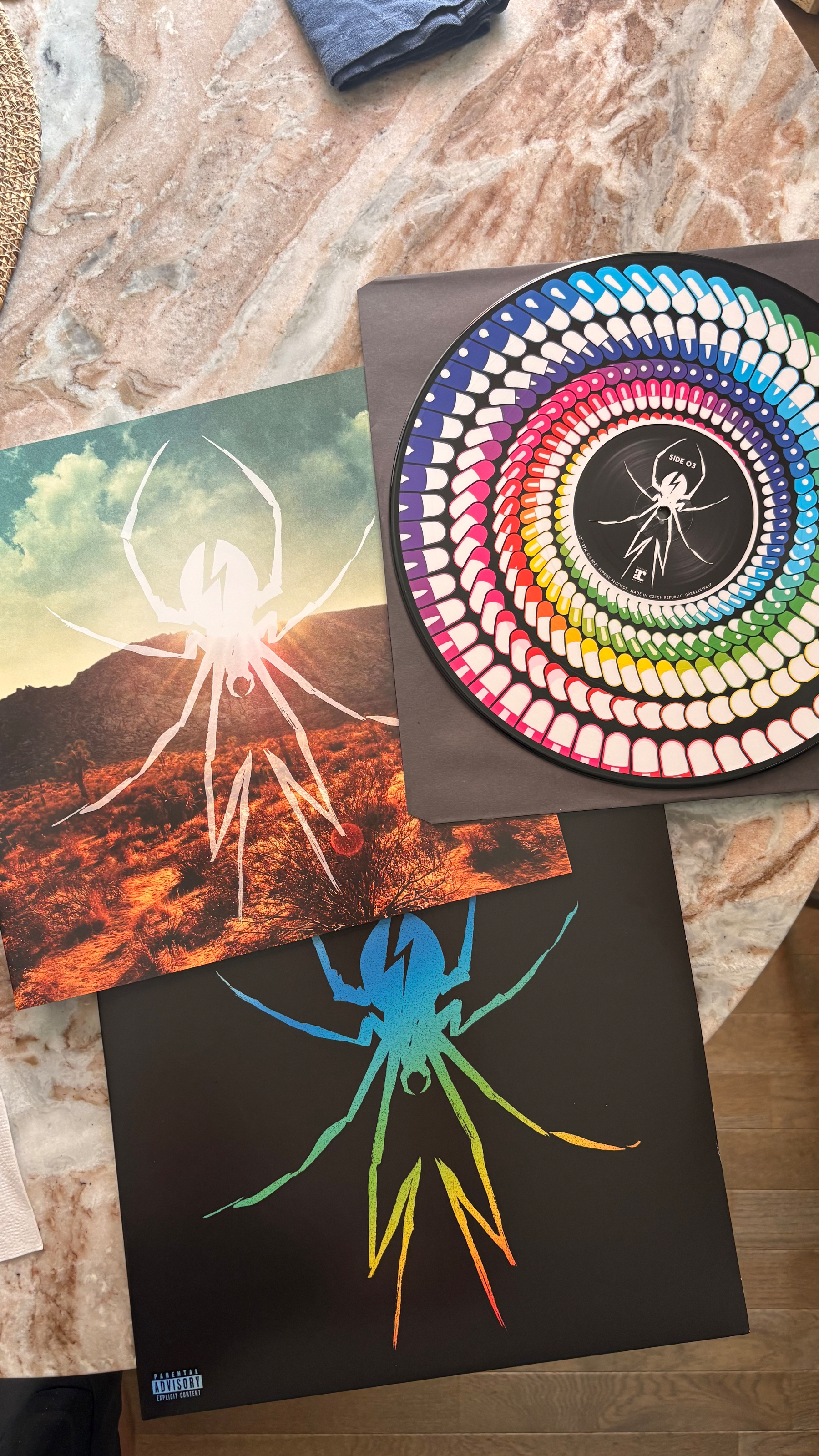 Several vinyl records and album covers featuring a spider logo with vibrant and colorful designs are displayed on a marble surface.
