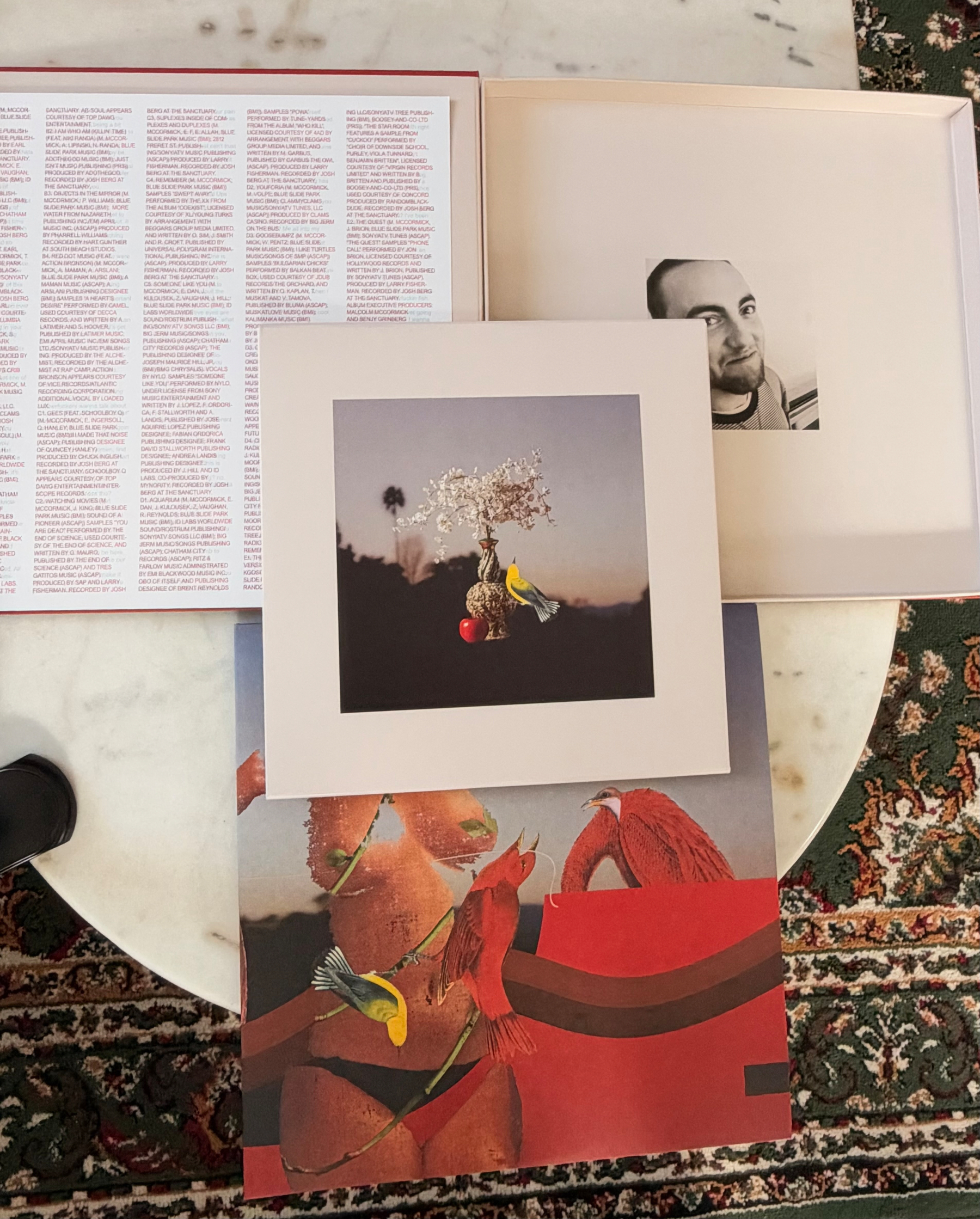 Auto-generated description: Several vinyl album covers with artistic illustrations and photographs are laid out on a round marble table.