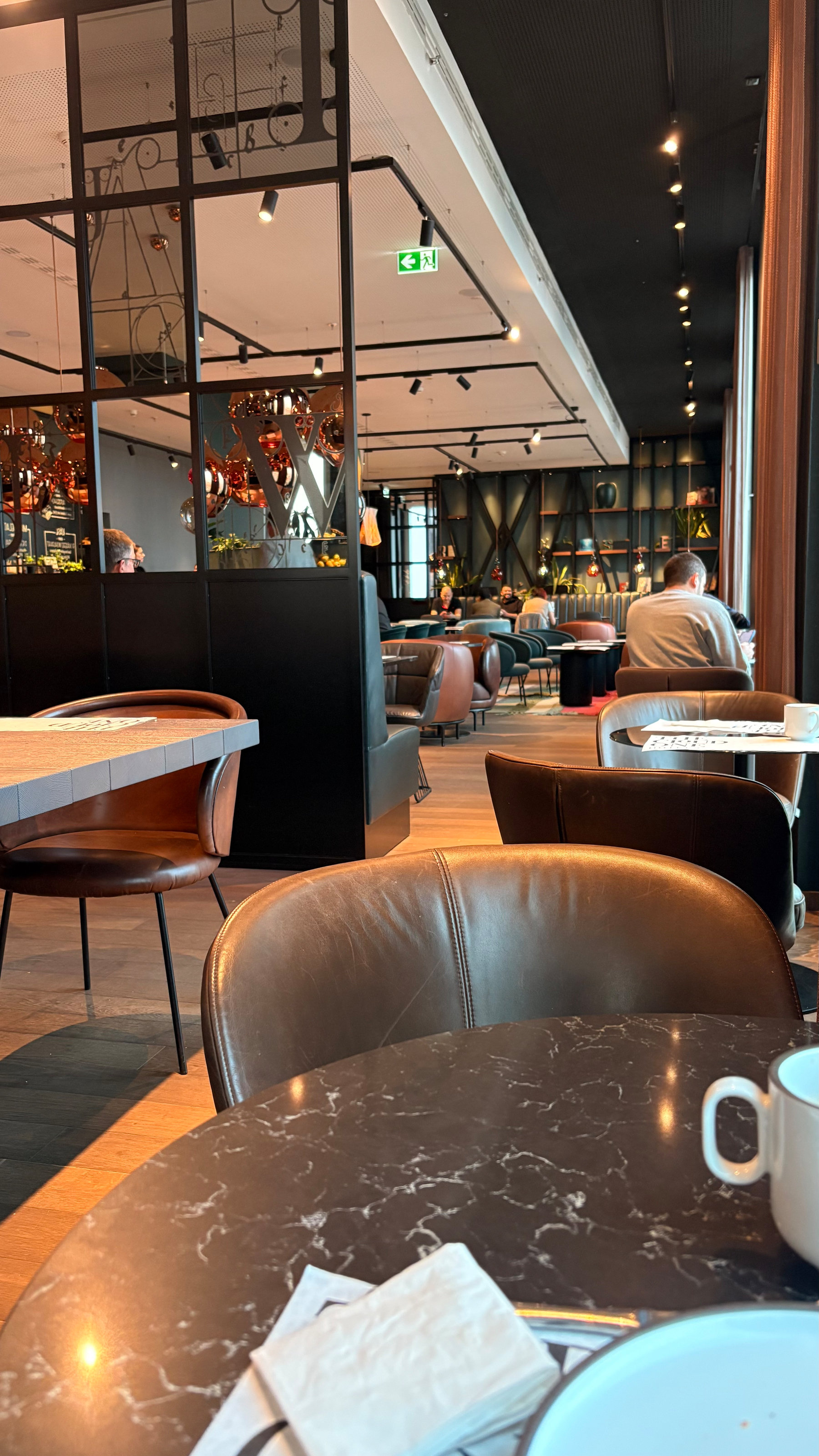 A modern, brightly lit café features cozy seating, marble tabletops, and a relaxed atmosphere with a few patrons seated inside.