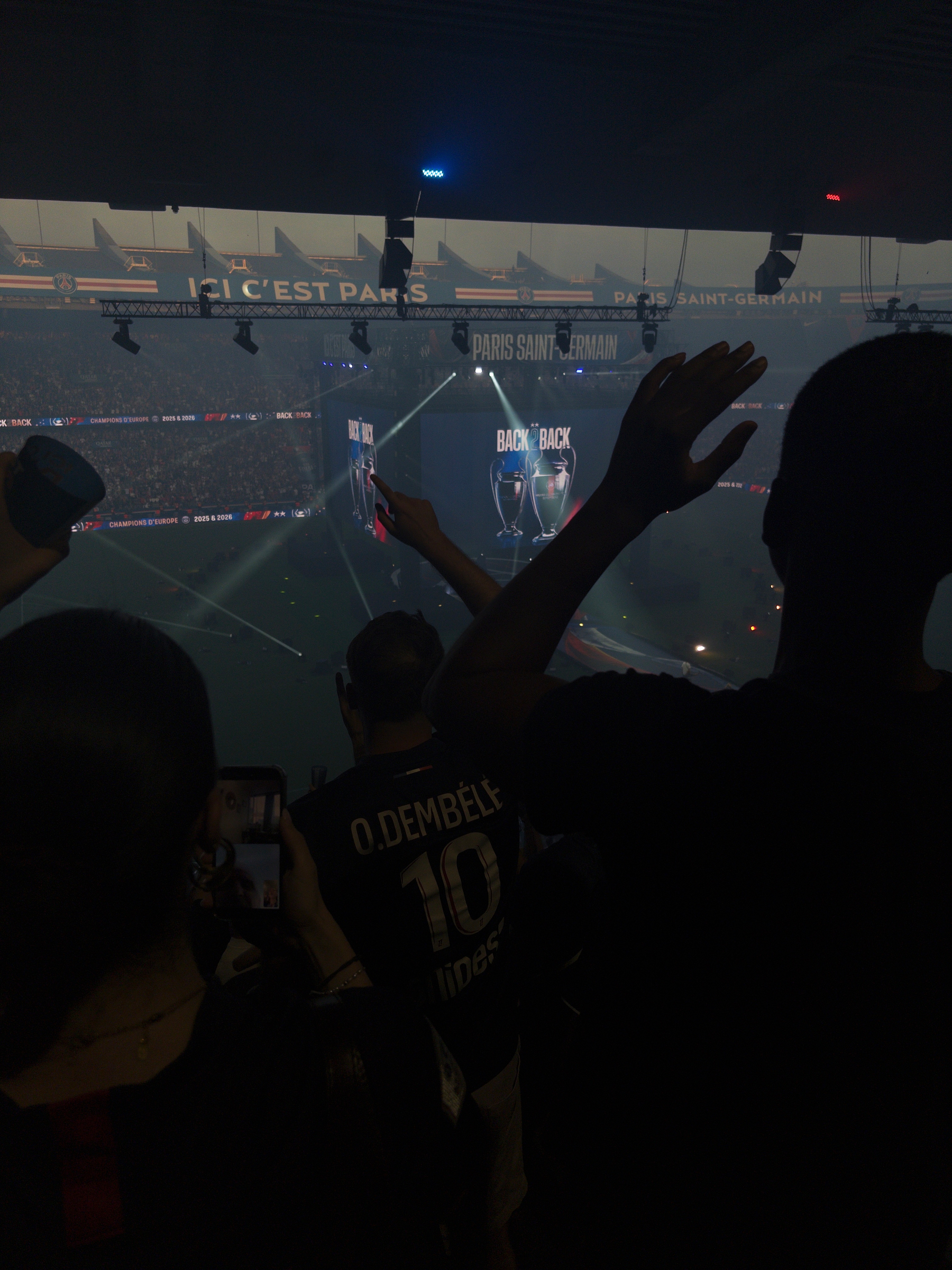 Fans inside a stadium cheer as a large screen displays a Back to Back message and images of trophies.