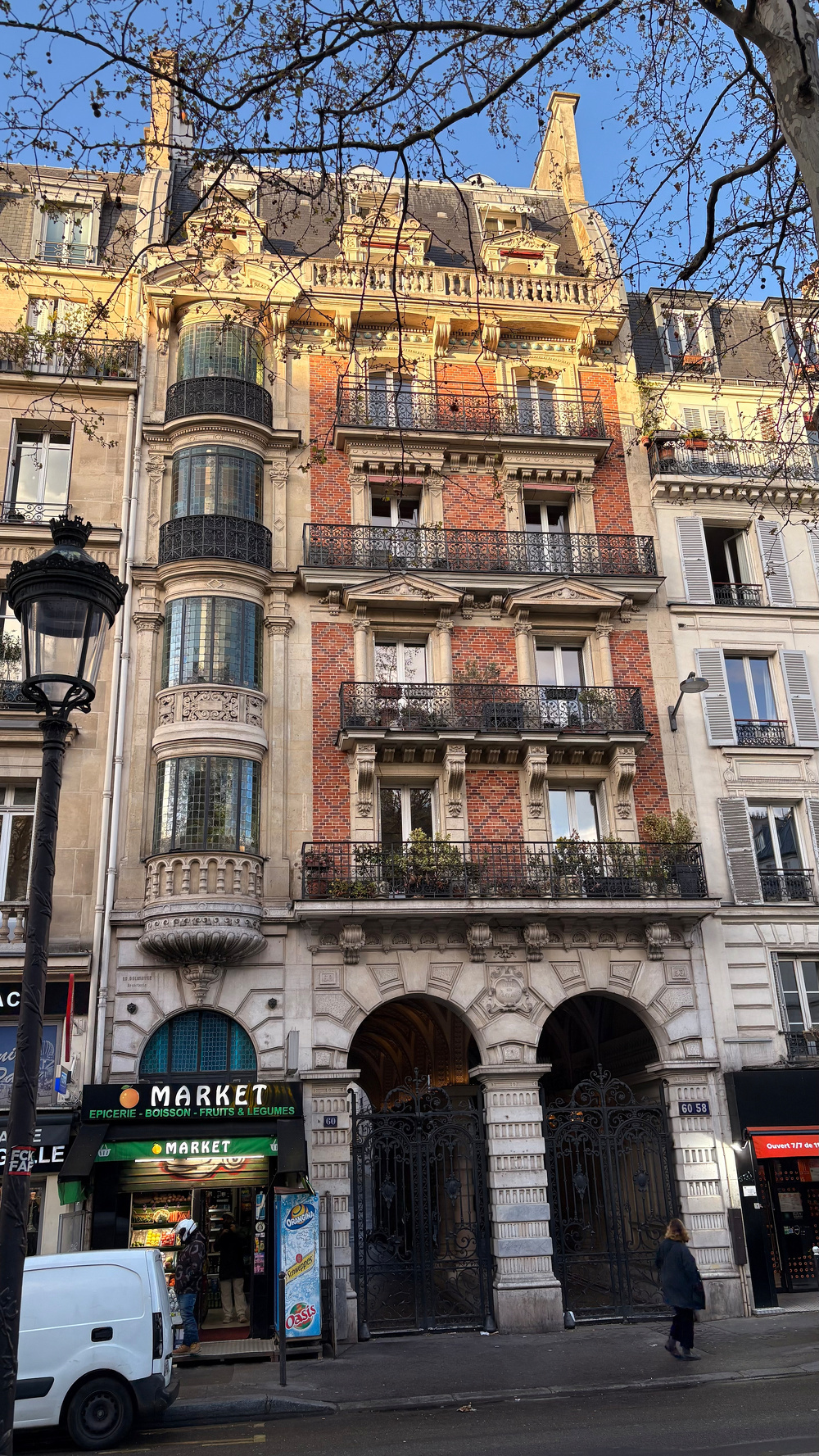 A historic multi-story building with ornate architecture features a small market on the ground floor, set against a clear blue sky.