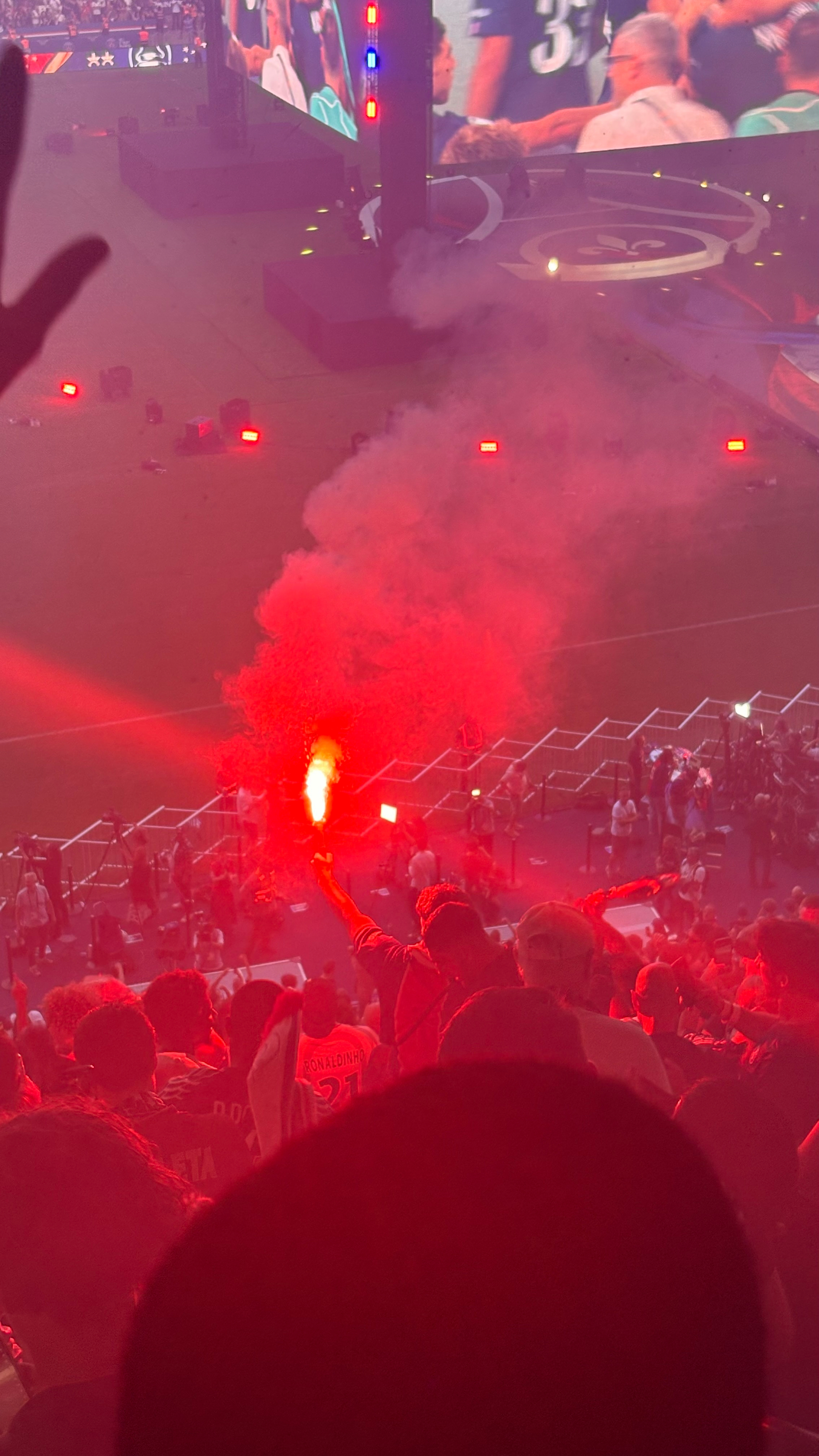 A person holds a red flare in a crowded stadium during an event or celebration.