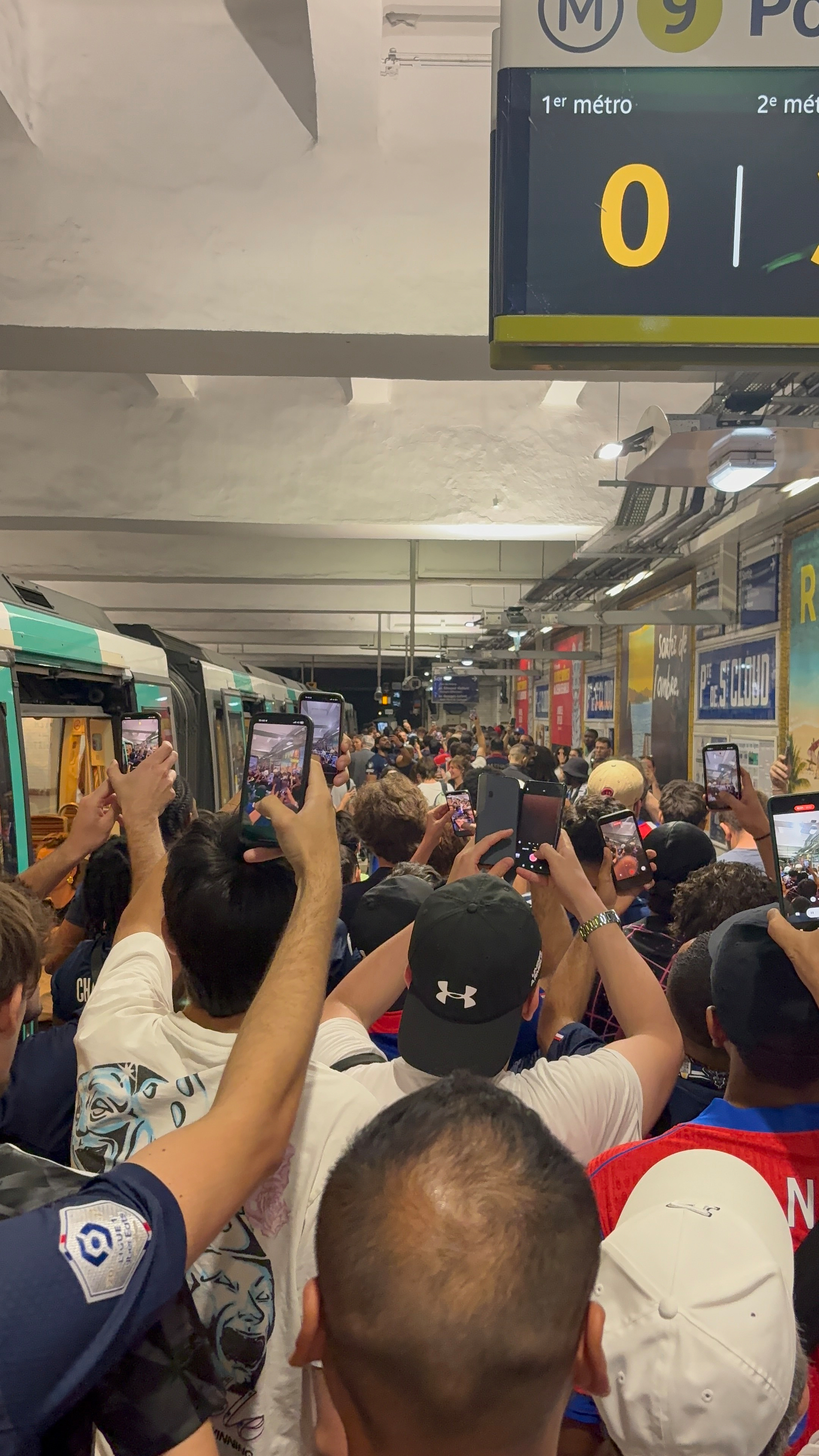 A crowd of people at a subway platform hold up their phones, possibly capturing a scene or event.