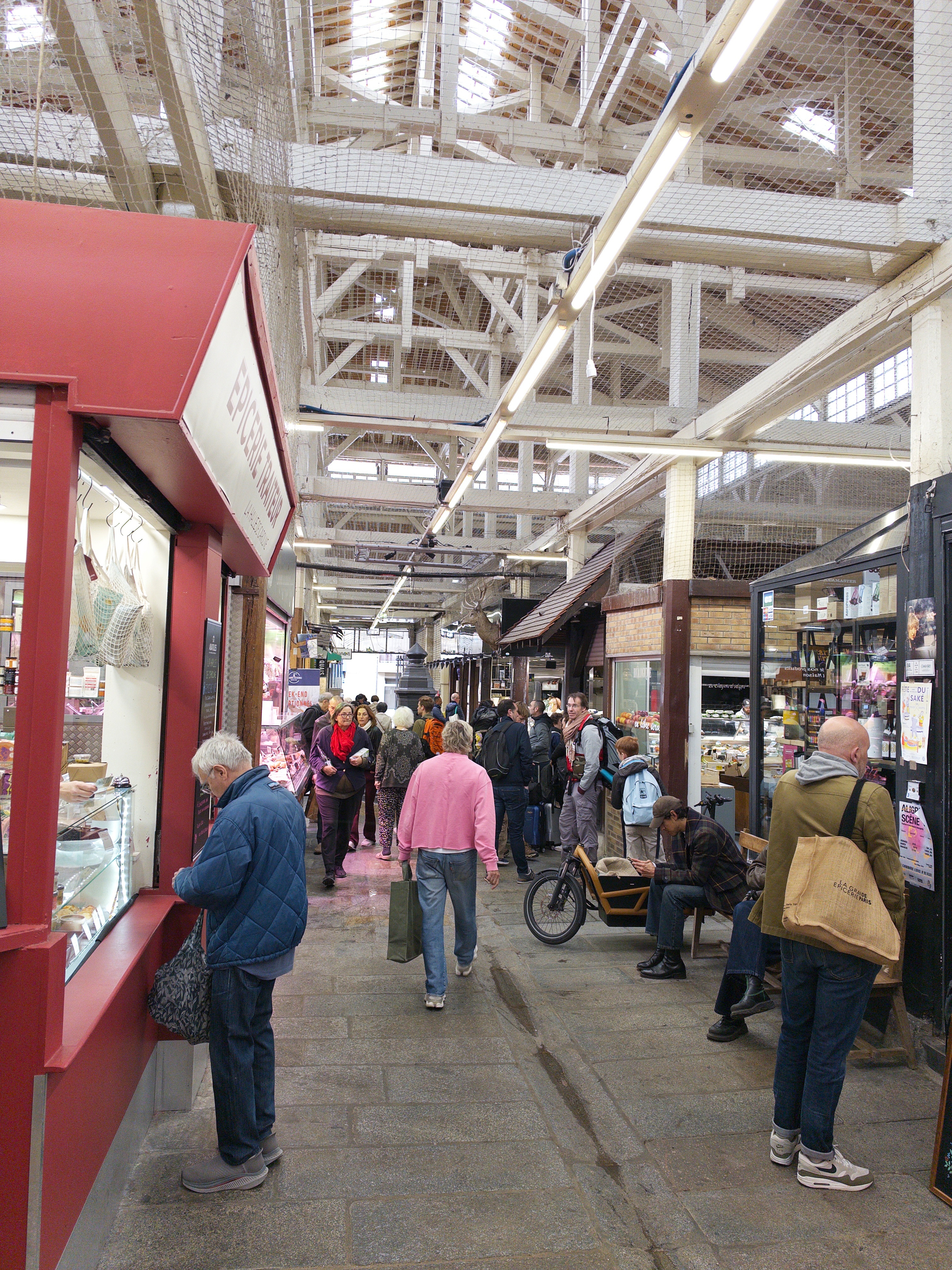 A busy indoor market with people shopping and walking along a pathway lined with various stalls and shops.