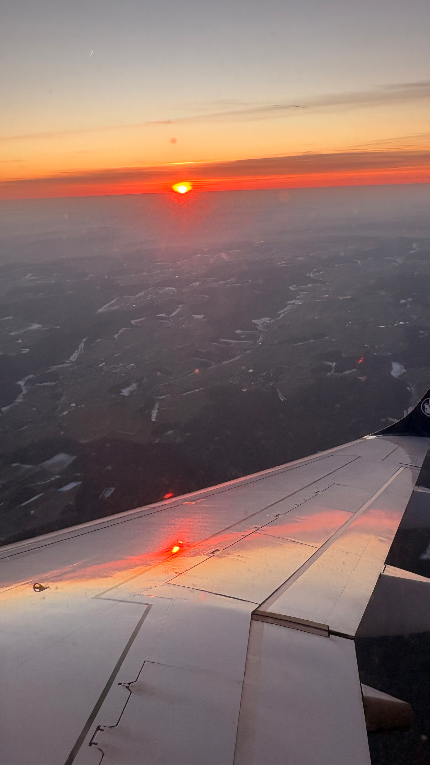 A sunset is seen from an airplane window, with the wing reflecting the vibrant hues of the sky.