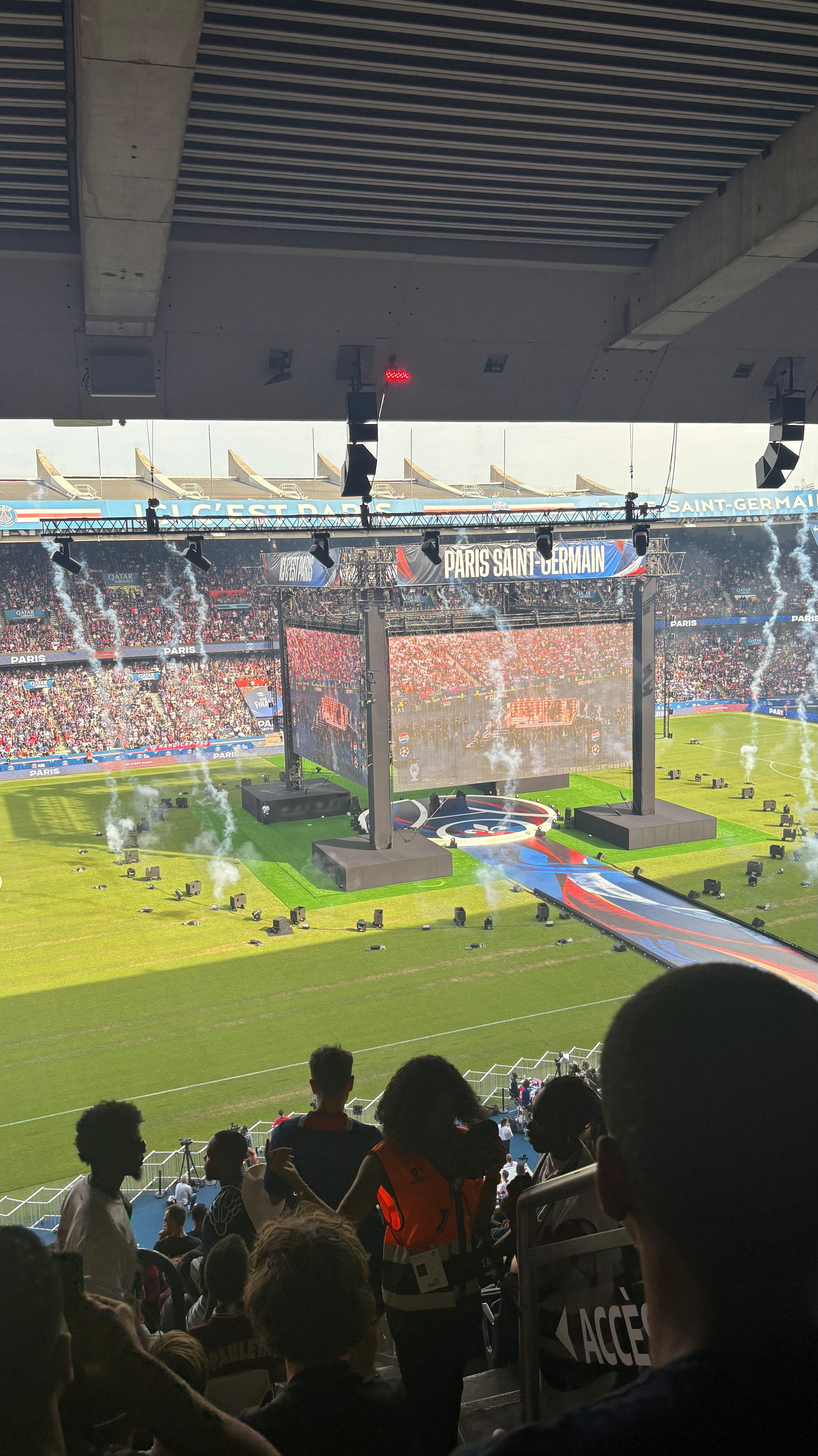A lively stadium scene at Parc des Princes features a large stage with Paris Saint-Germain on screen and an enthusiastic crowd.