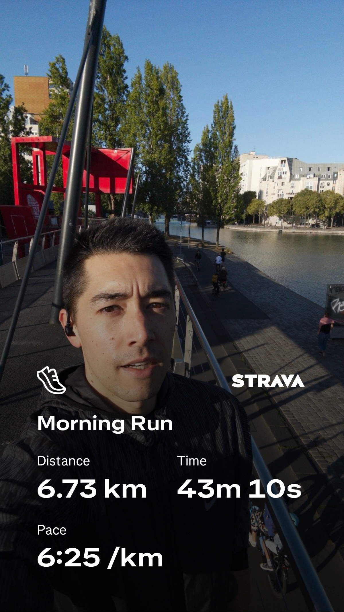 A man wearing earphones is taking a selfie on a bridge near a river during a morning run, with Strava stats showing a distance of 6.73 km, time of 43 minutes 10 seconds, and a pace of 6:25 per km.