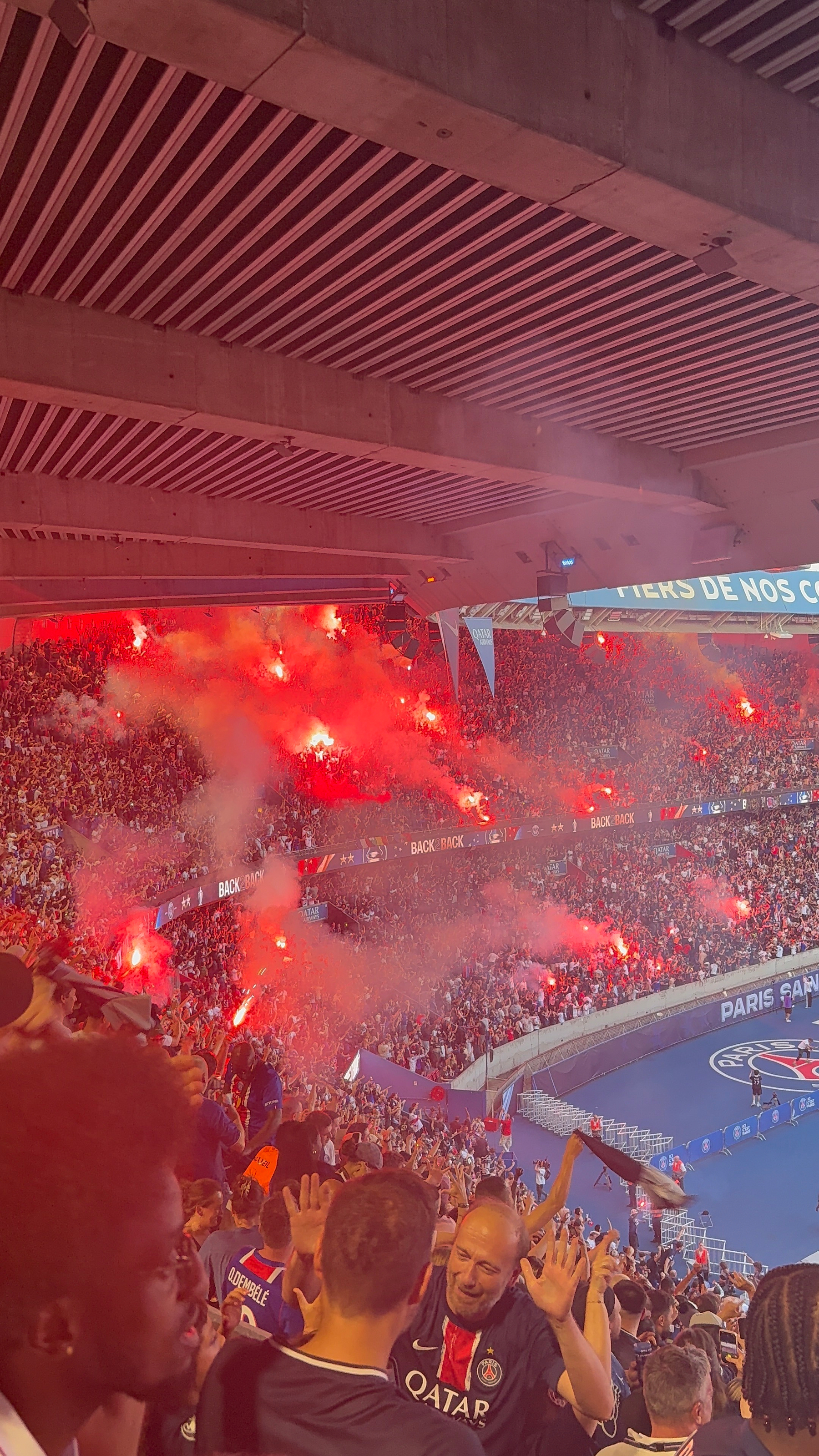 Fans at a stadium are energetically celebrating with red flares, creating a lively atmosphere.