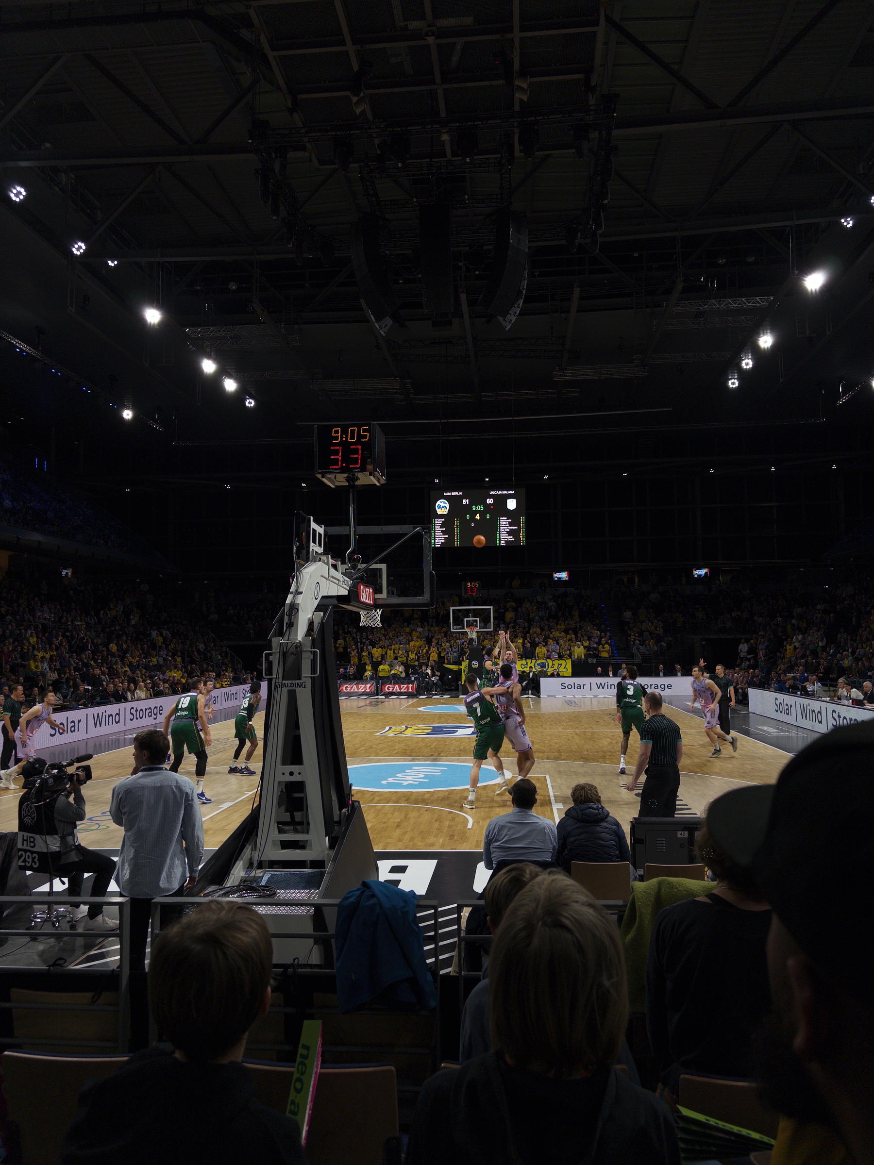 Auto-generated description: A basketball game is being played in an indoor arena with a crowd watching from the stands.