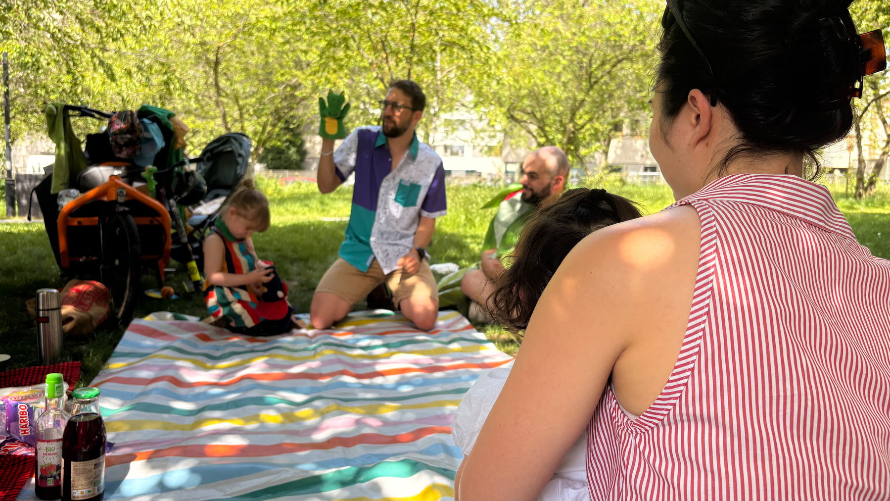 A group of people are enjoying a picnic on a colorful striped blanket in a sunny park.