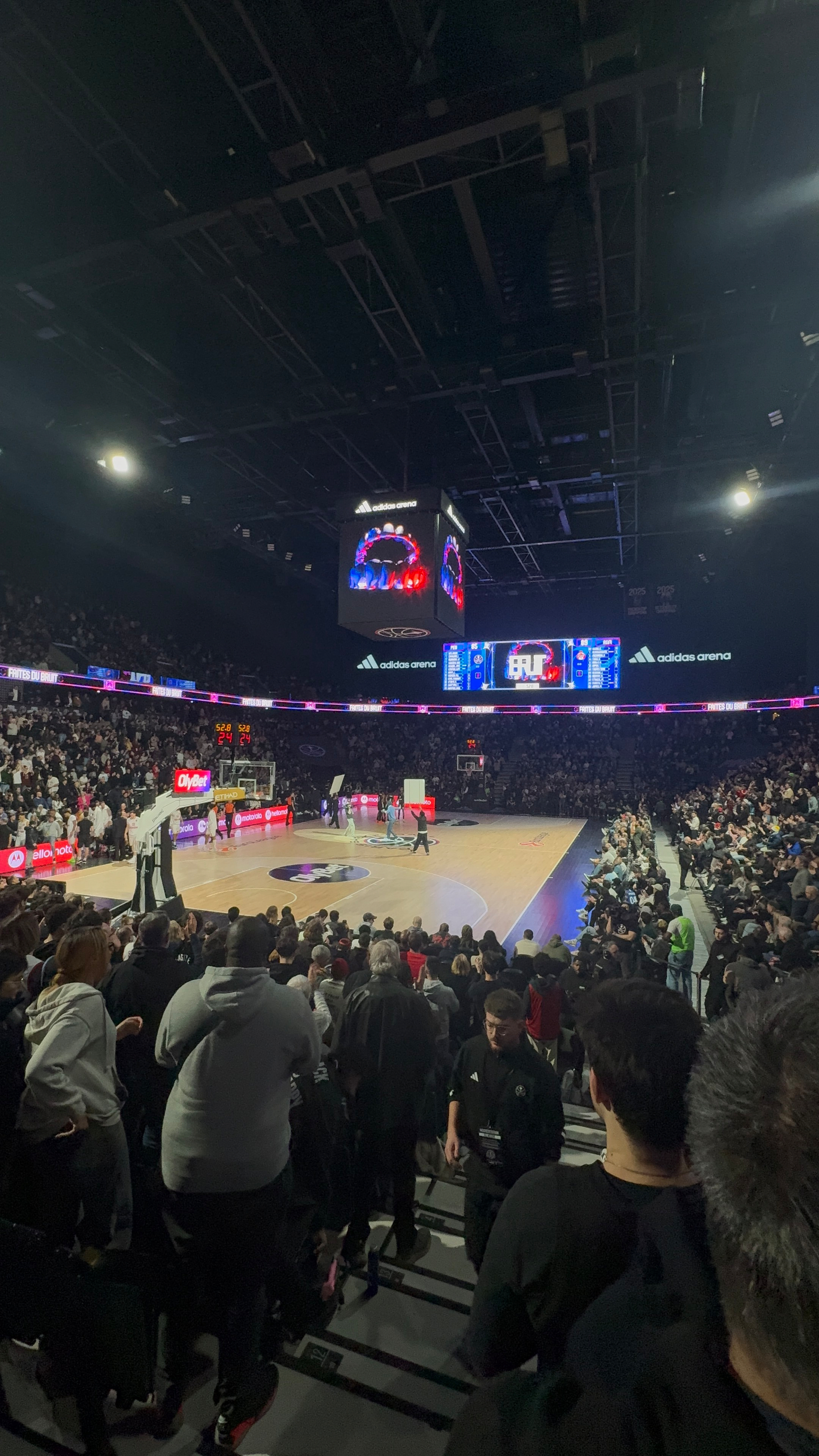 A crowded basketball arena has spectators watching an ongoing game with a vibrant scoreboard and court.