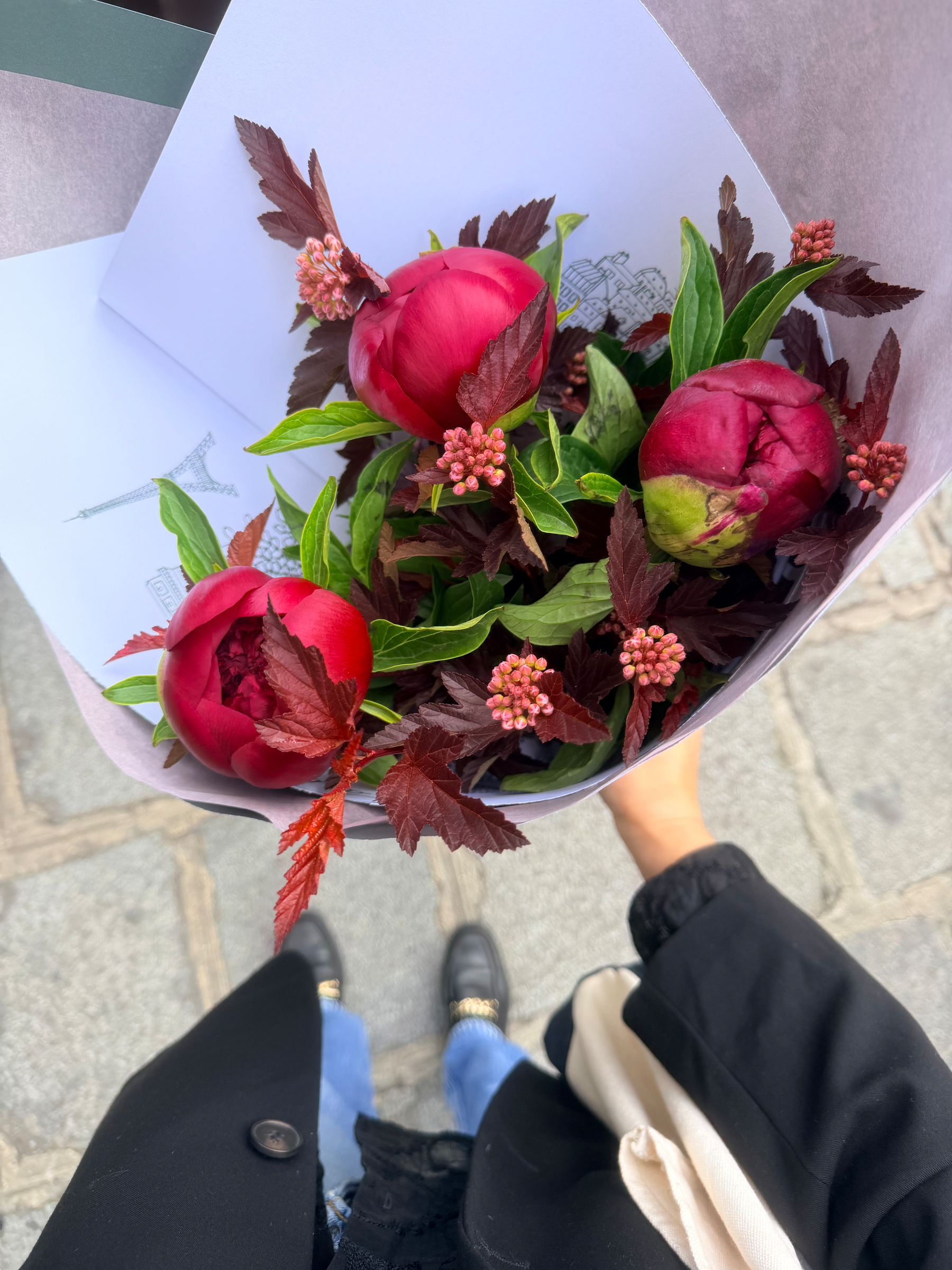 Auto-generated description: A bouquet of vibrant red flowers with greenery and small pink buds is held over a city street.