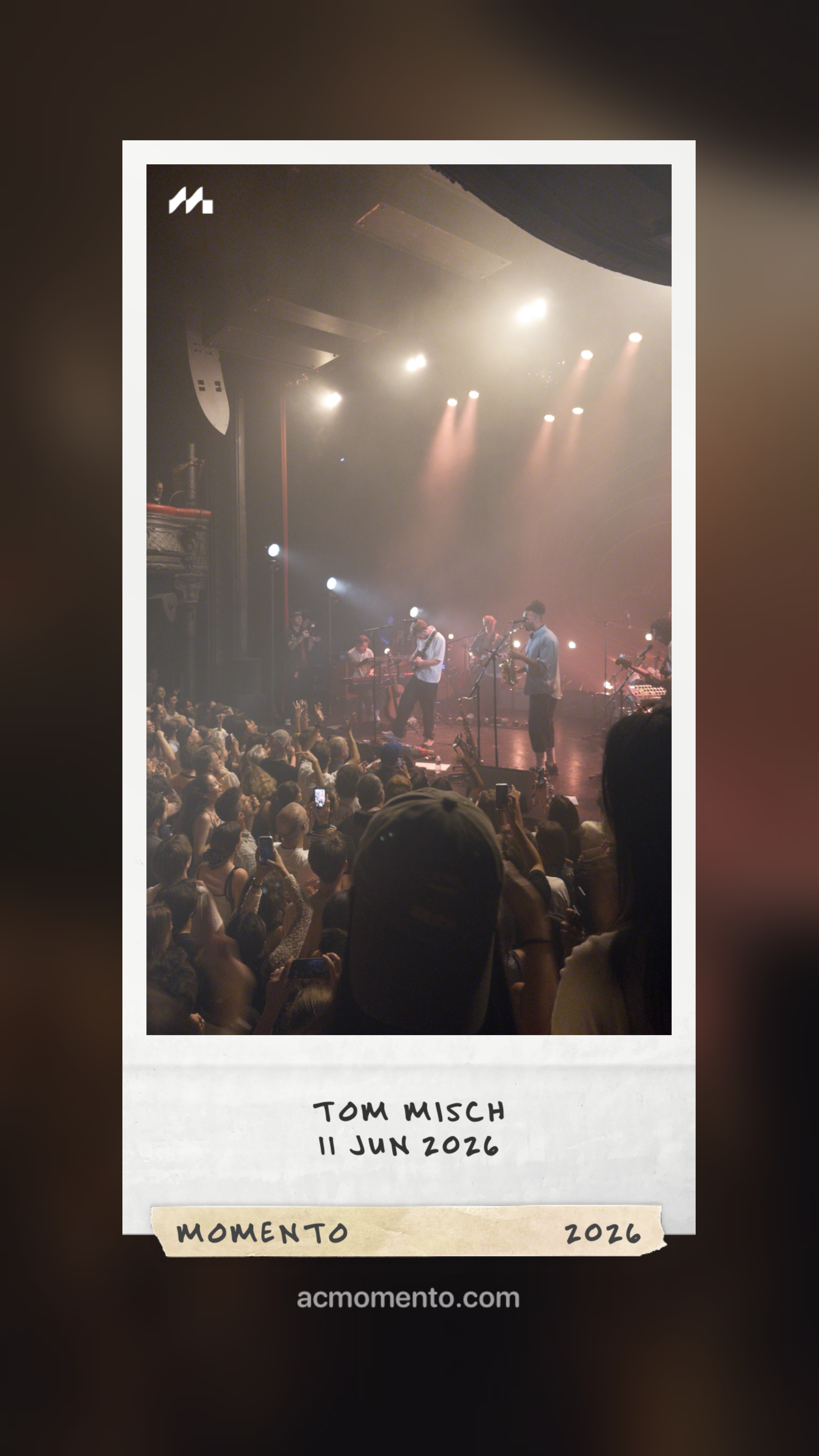 A live concert with musicians performing on stage and a crowd watching, framed as a Polaroid photo with TOM MISCH 11 JUN 2026 written at the bottom.