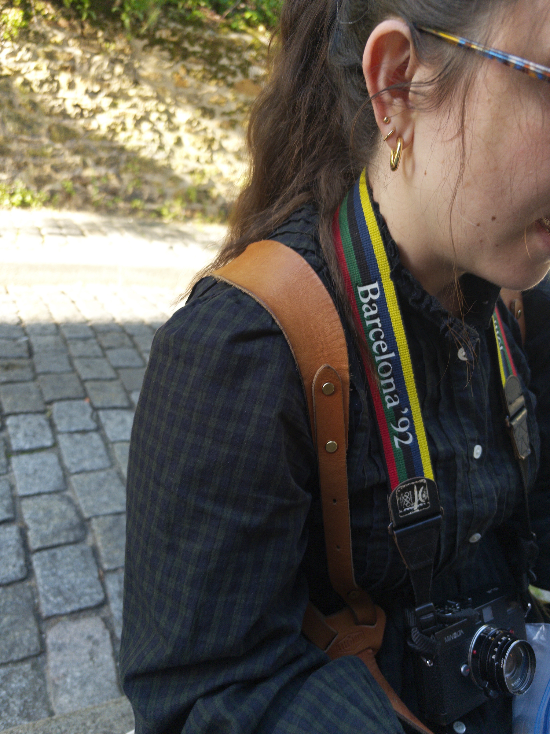 Auto-generated description: A person wearing a jacket and a camera strap labeled Barcelona '92 is sitting on a stone surface.