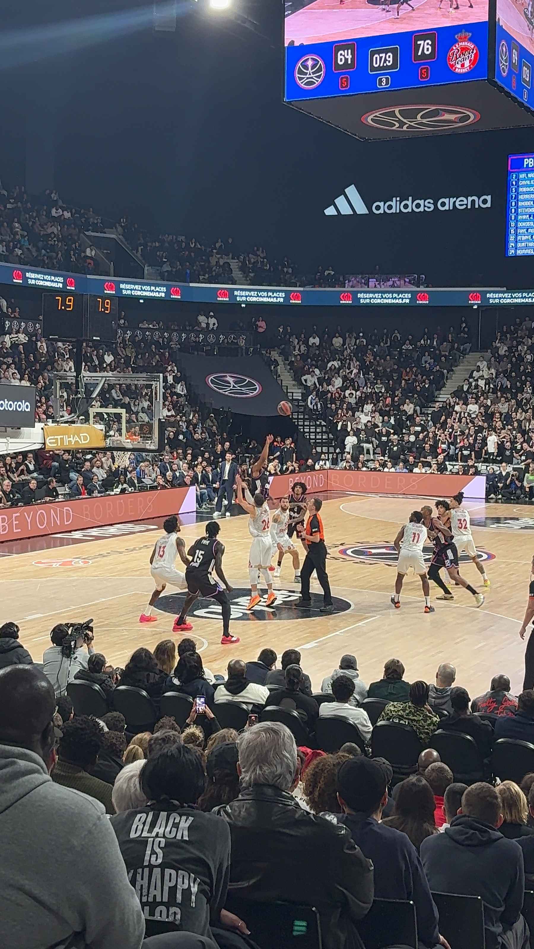 A basketball game is taking place in a packed arena, with players on the court actively engaged and spectators watching intently.