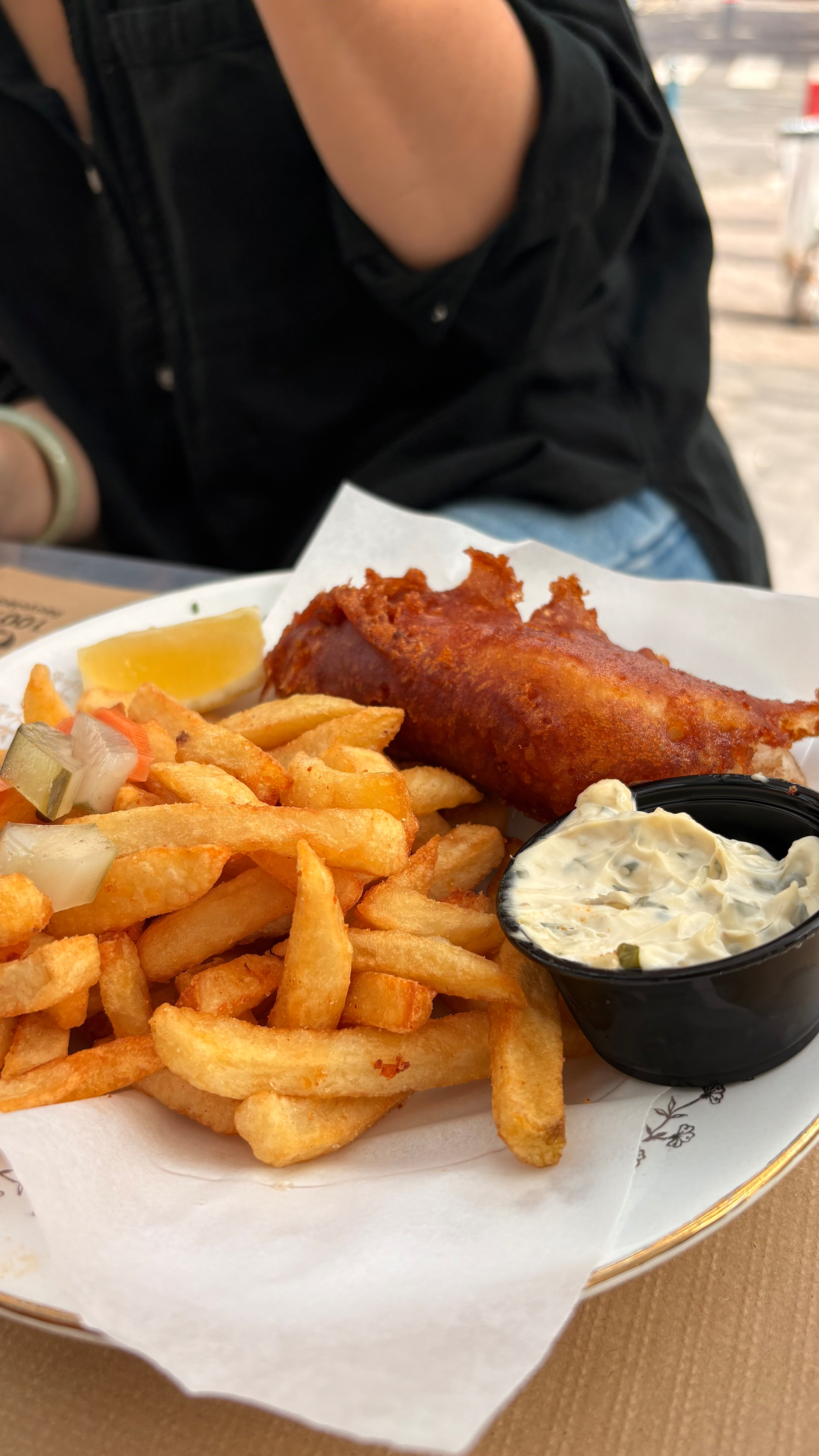 A plate of crispy fish and golden fries is served with a lemon wedge and tartar sauce.