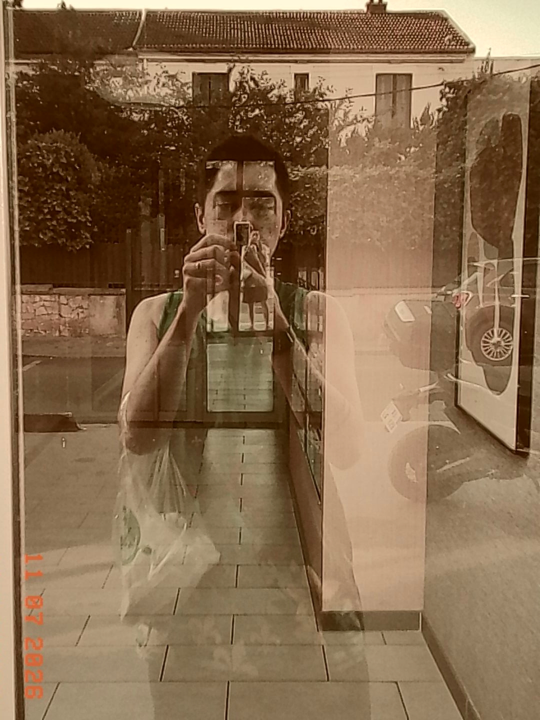 A person is taking a photograph of their reflection in a glass window or door, capturing both the interior and exterior scenes simultaneously.