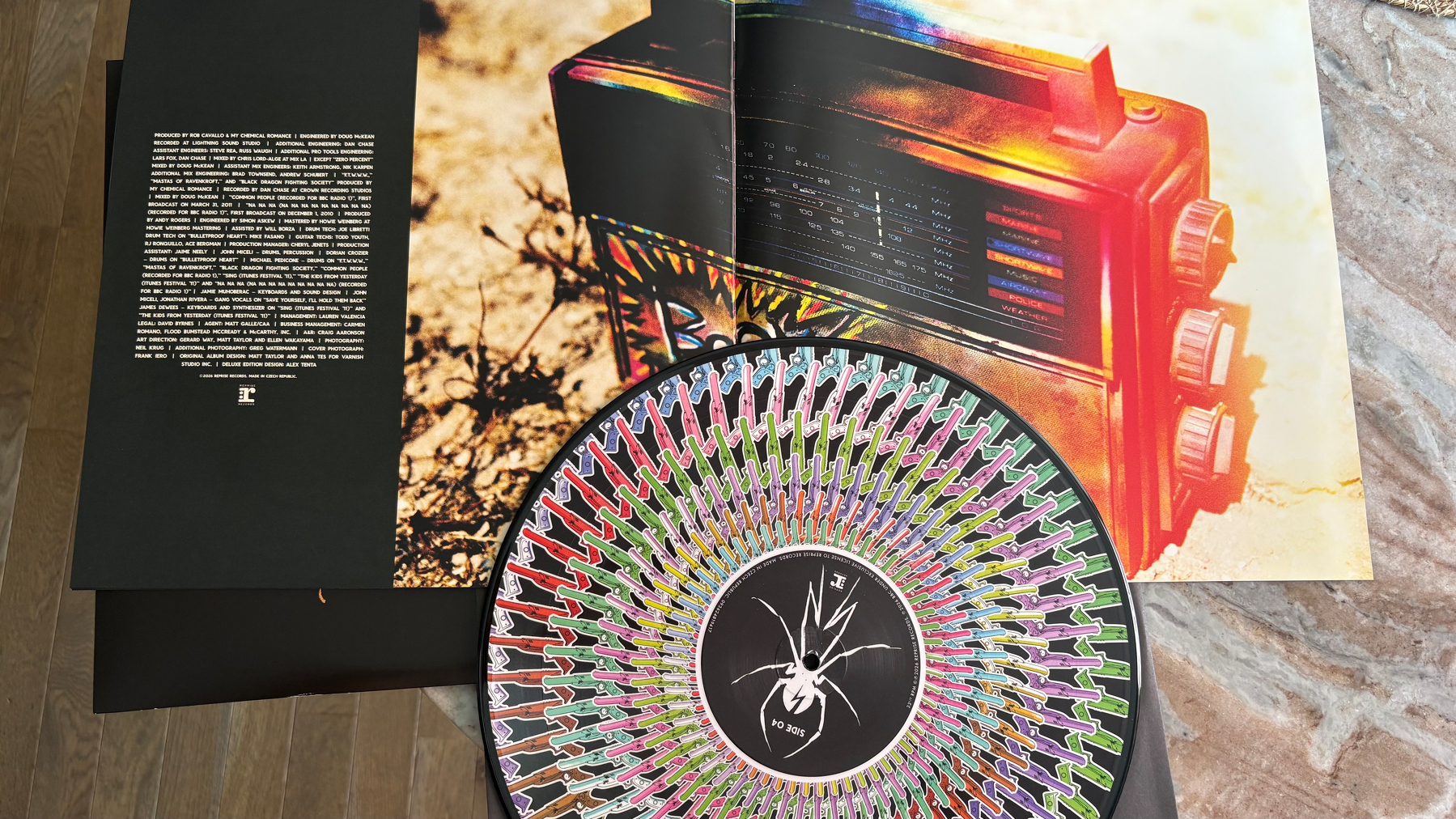 A vinyl record with colorful spider-themed artwork on its cover is placed on top of an open magazine featuring a retro radio.
