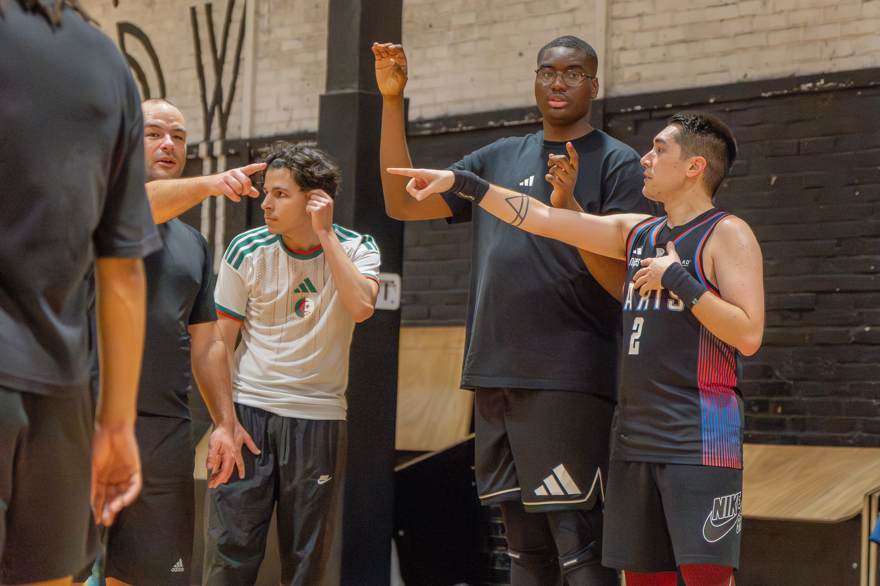 People are engaged in a lively discussion or game on a basketball court, with some pointing and gesturing.