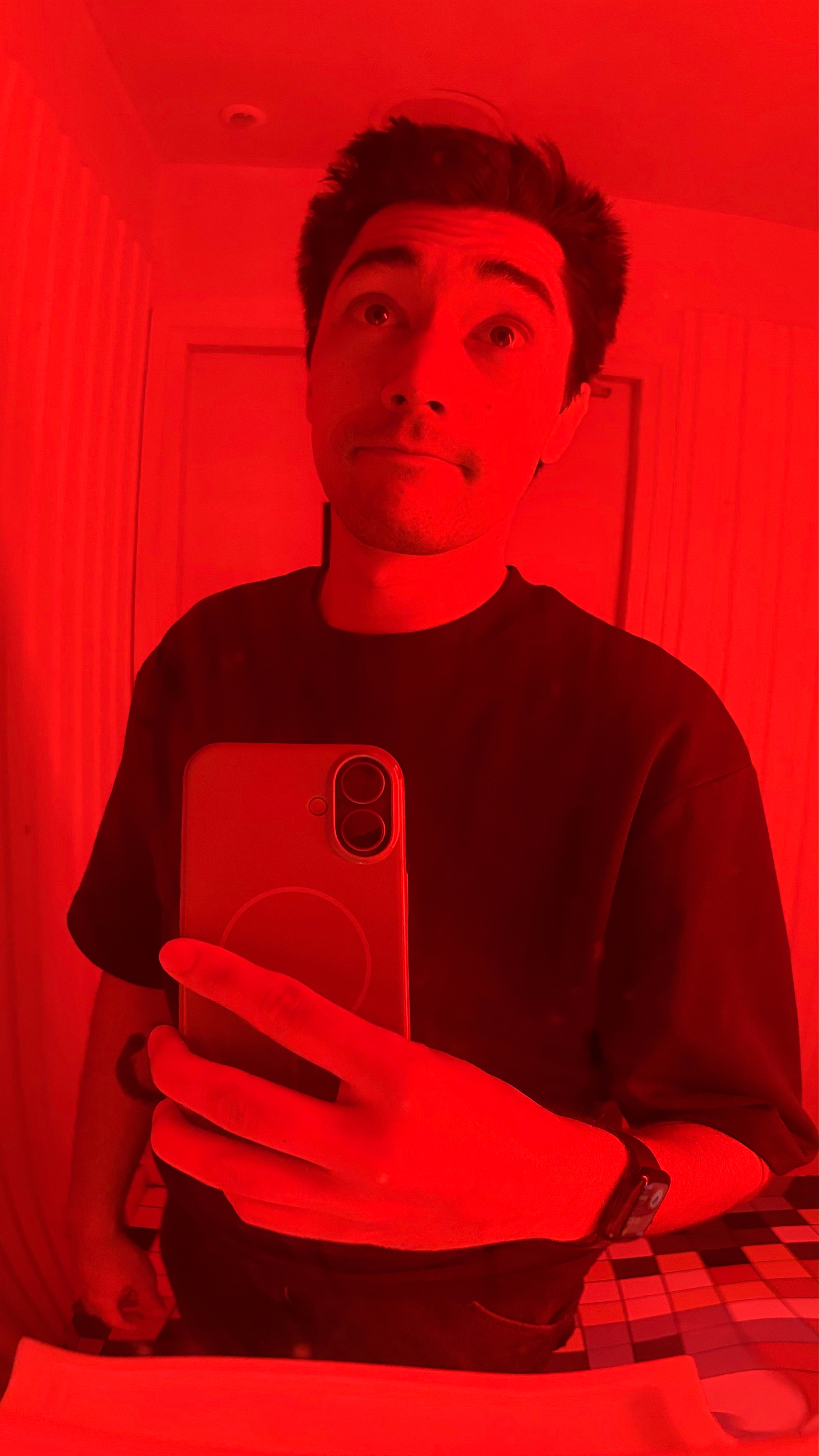 A person is taking a mirror selfie in a room illuminated with red light.