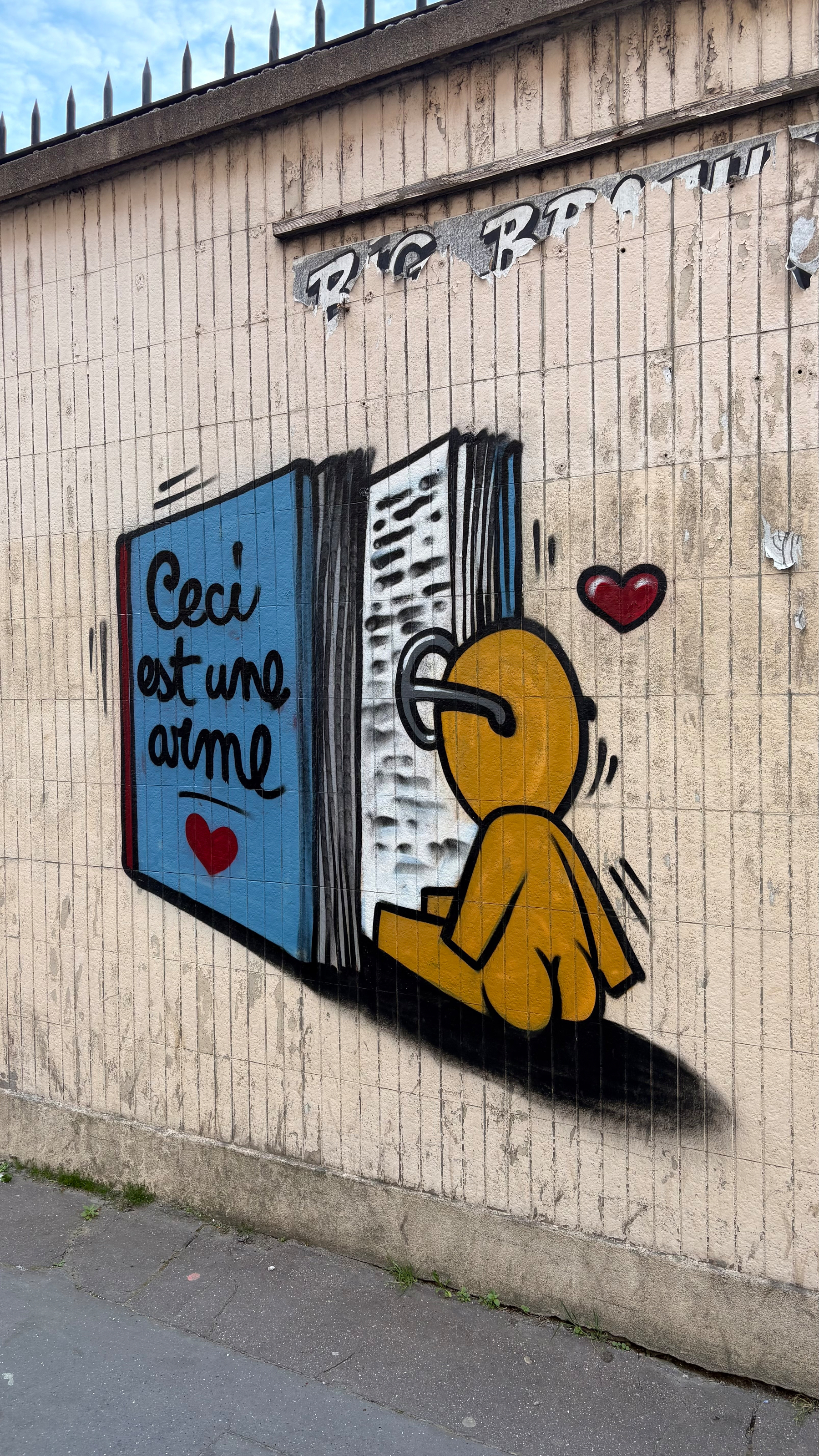 A mural on a wall depicts a figure interacting with a book, accompanied by the phrase Ceci est une arme and a heart symbol.