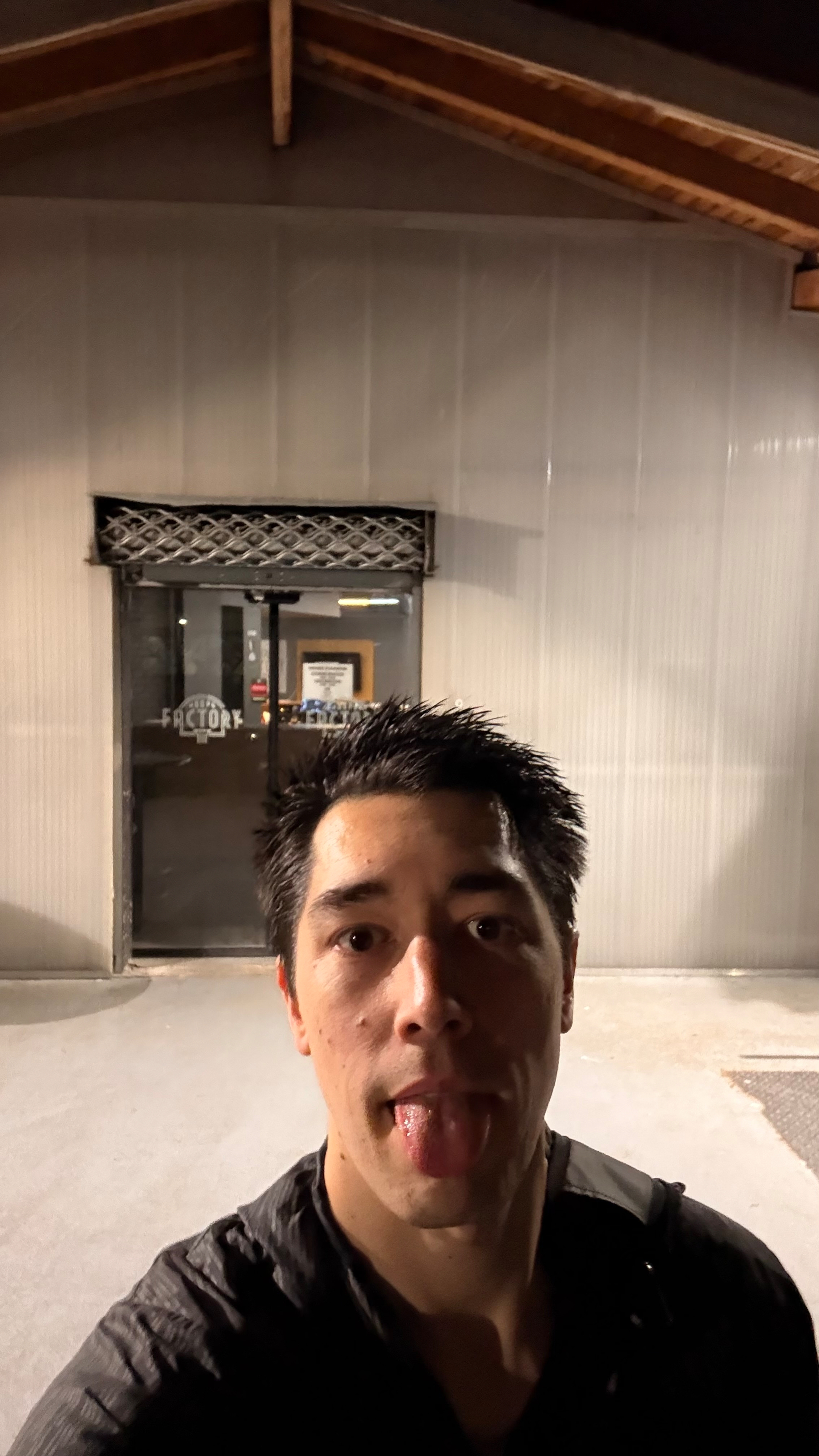 Auto-generated description: A person is taking a selfie outside a building at night.