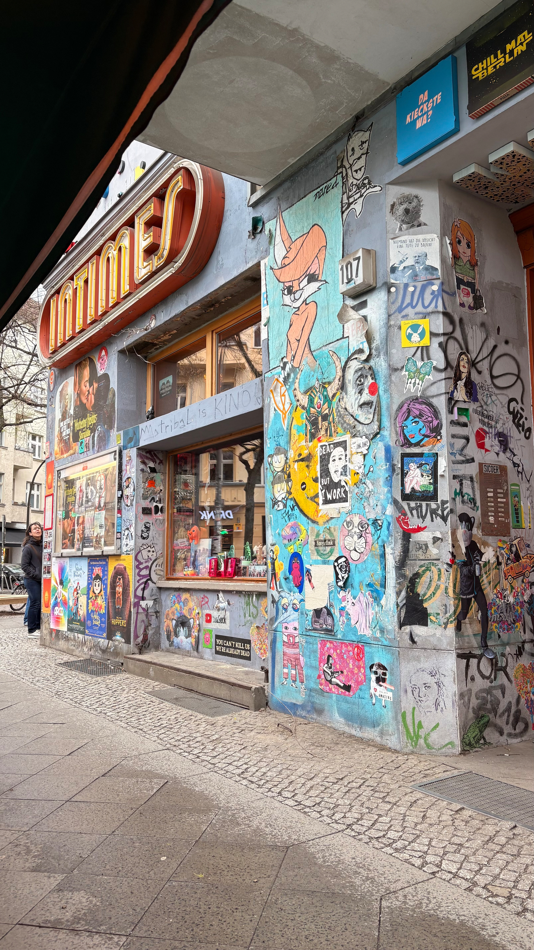 Auto-generated description: A graffiti-covered urban building corner features vibrant street art, posters, and a variety of stickers.