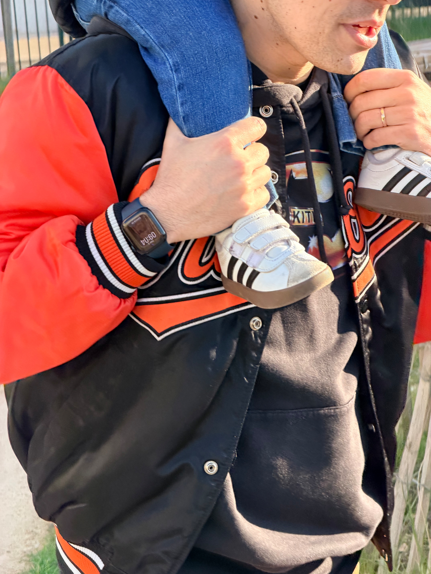 A person is carrying someone on their shoulders, wearing a black and orange jacket and a smartwatch.