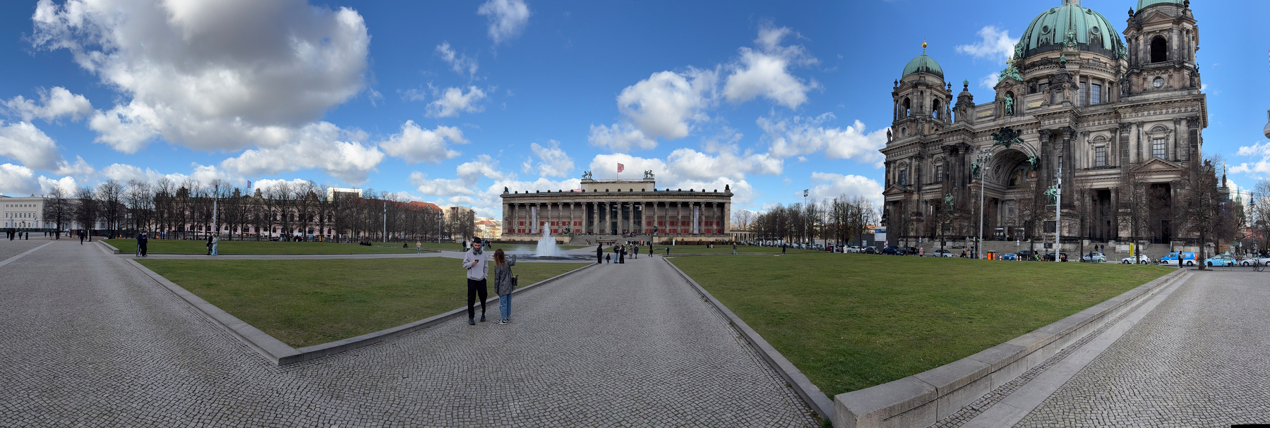 Auto-generated description: A large open plaza features lush green lawns flanked by historic buildings, including a grand cathedral on one side.